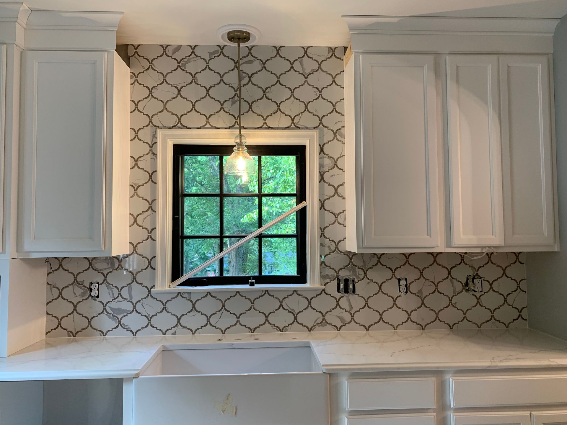 Kitchen with white cabinets, patterned backsplash, and window over a white farmhouse sink.