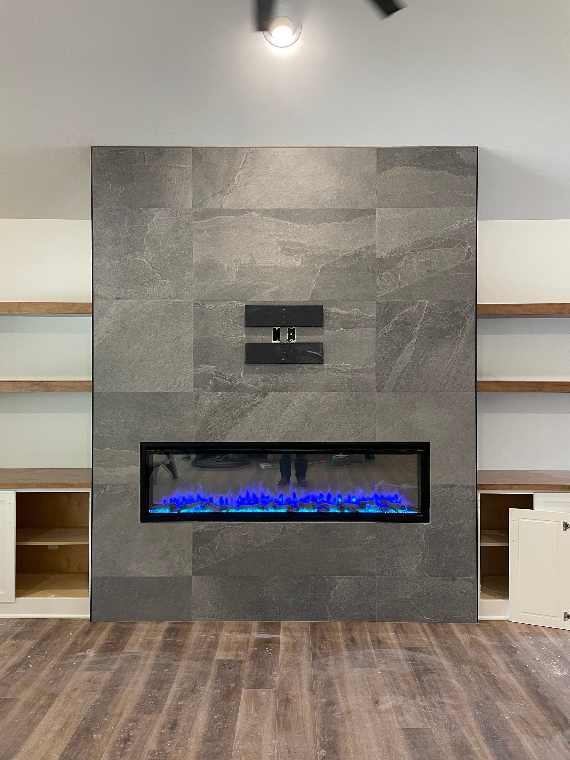 A fireplace with blue flames, set in a grey tiled wall. Built-in shelves and cabinets flank the feature.