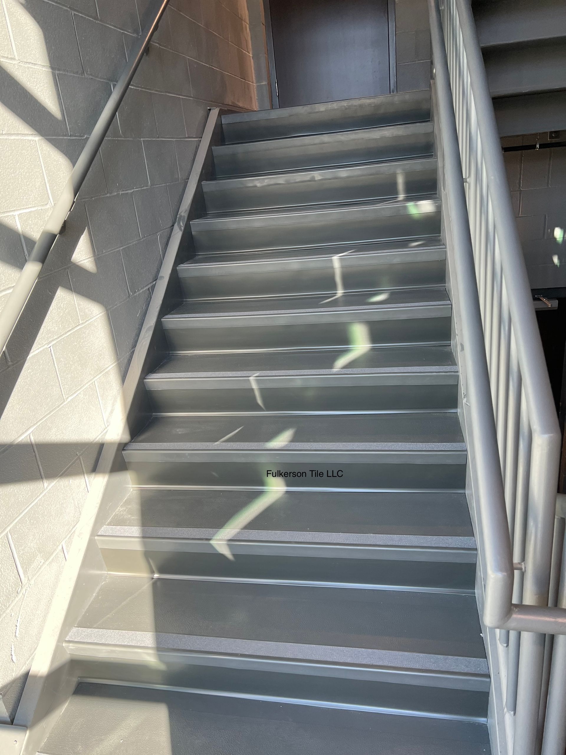 Staircase with metal steps, handrail, and sunlight streaming down.