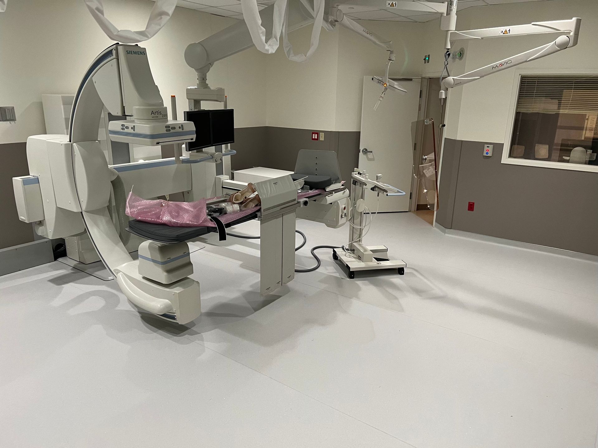 Angiography room with a large medical imaging machine and equipment; white and gray color scheme.