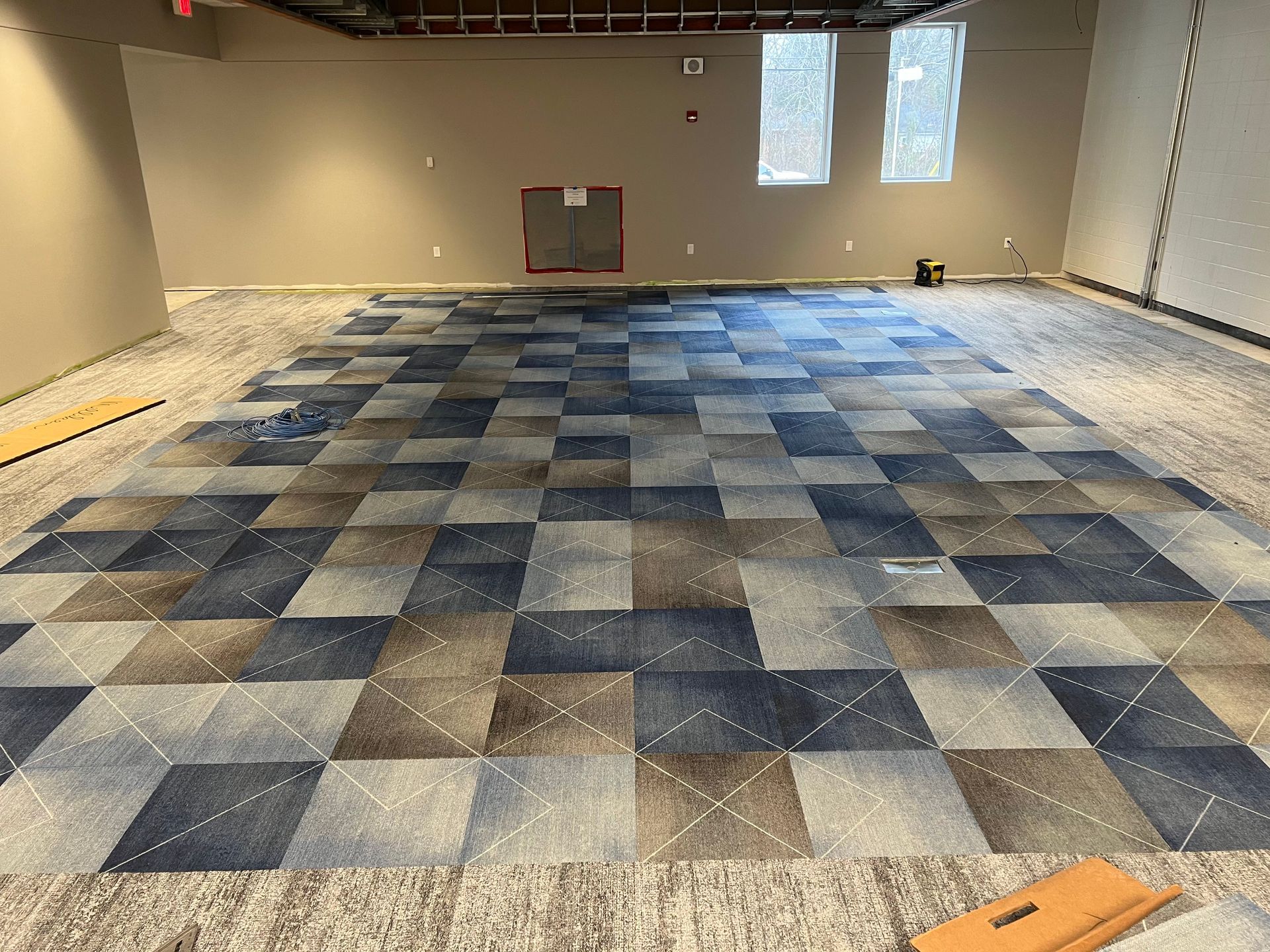 Carpet tile installation in a room. Blue, brown and grey squares on the floor, unfinished walls.