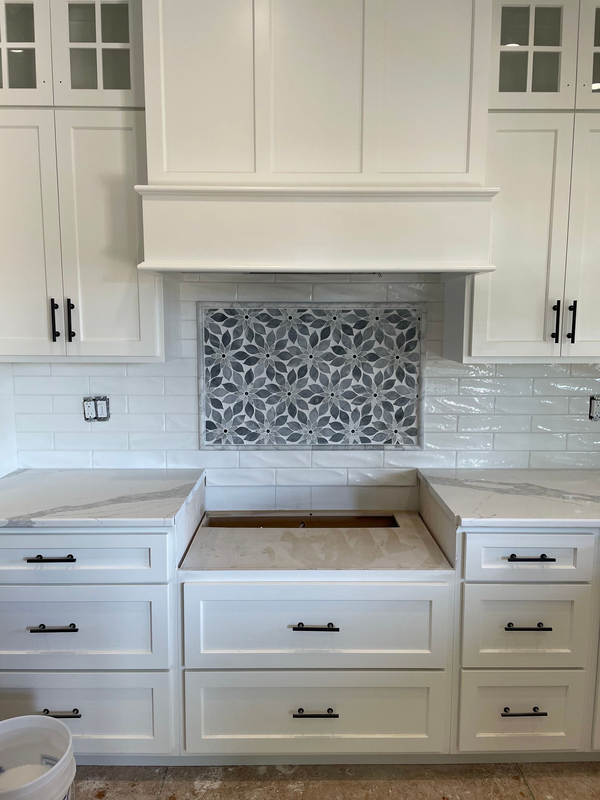 White kitchen with cabinets, marble countertops, patterned backsplash, and range hood.