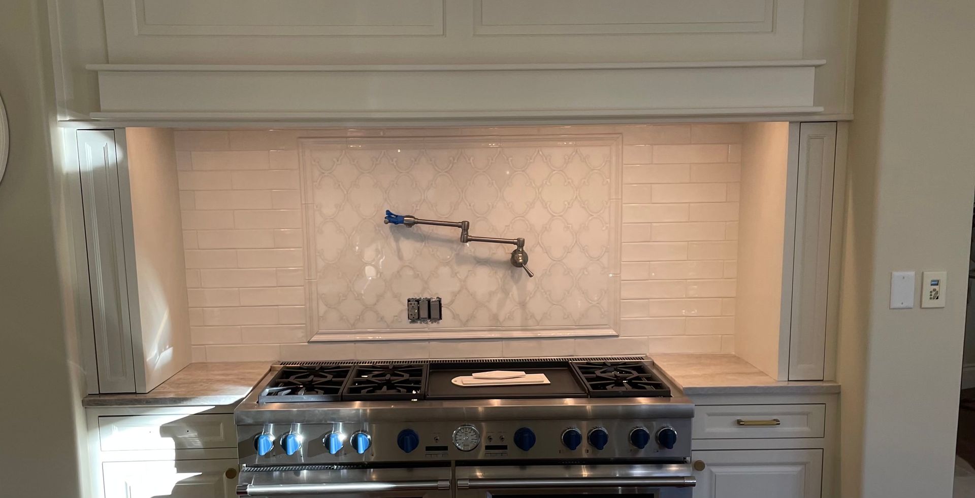 Kitchen with stainless steel range, white cabinets, patterned backsplash, and a pot filler faucet.