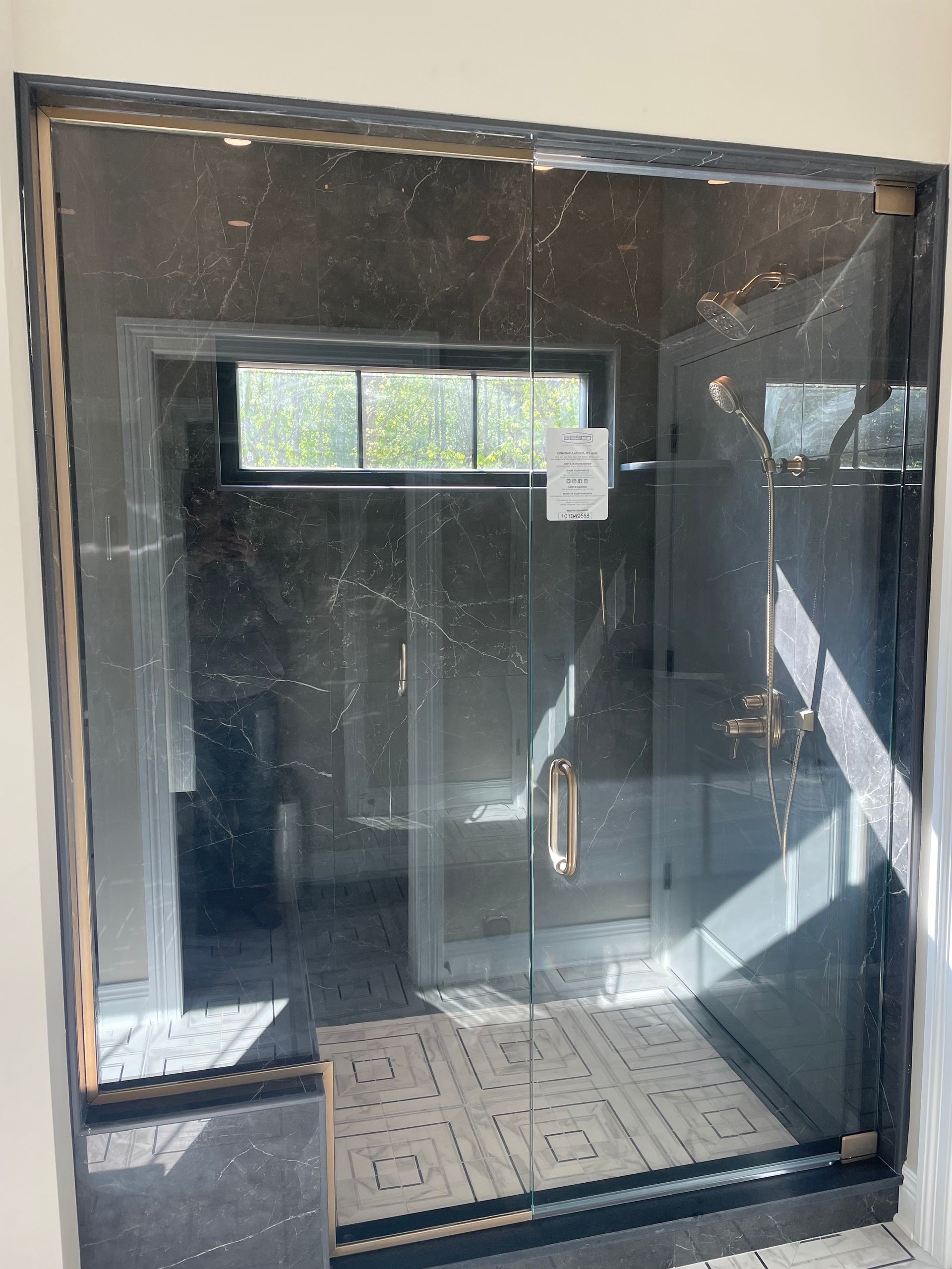 Glass shower enclosure with black trim, tile floor, and brass hardware.