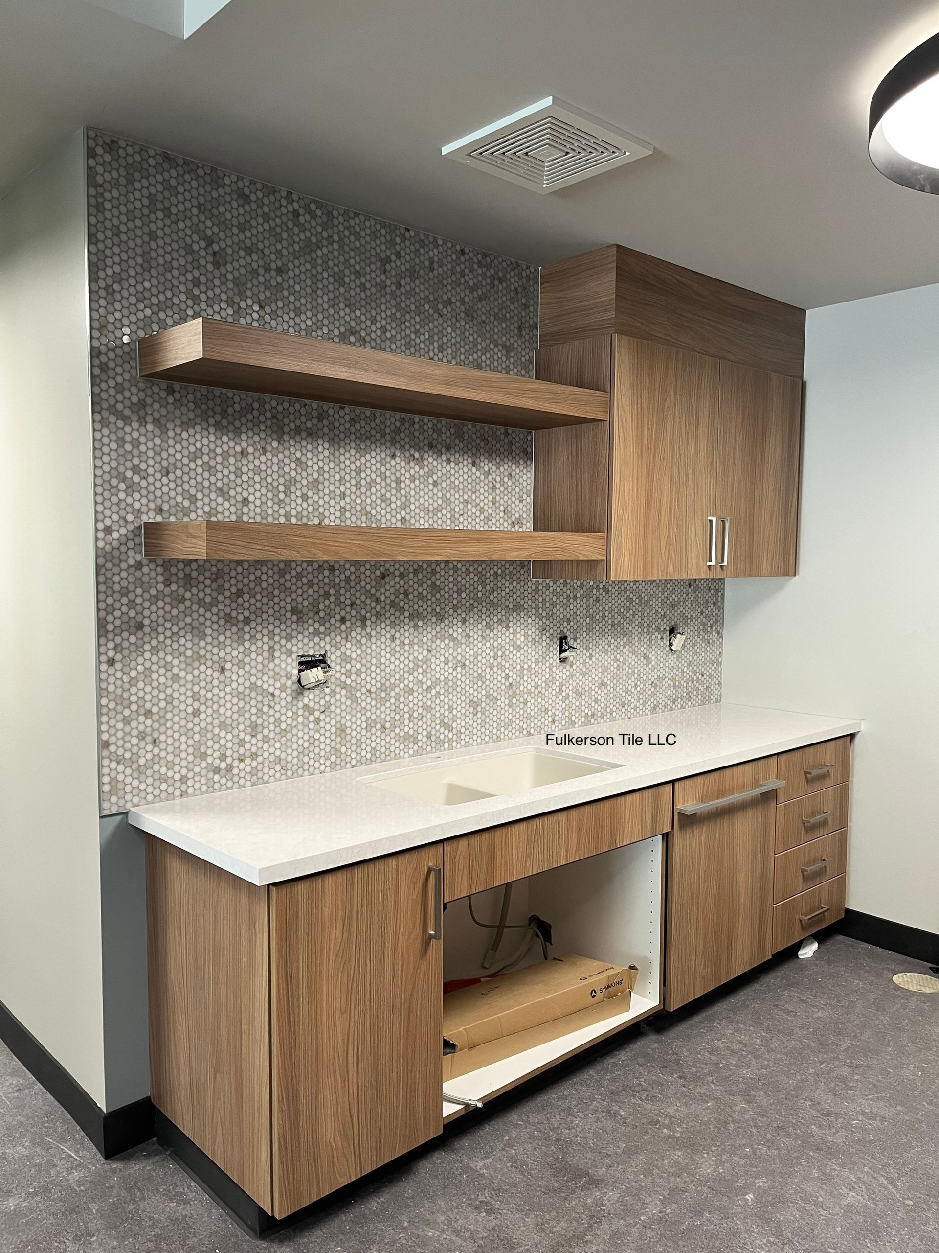 Built-in cabinet with countertop, sink, and upper shelving in a room with textured wall and gray floor.