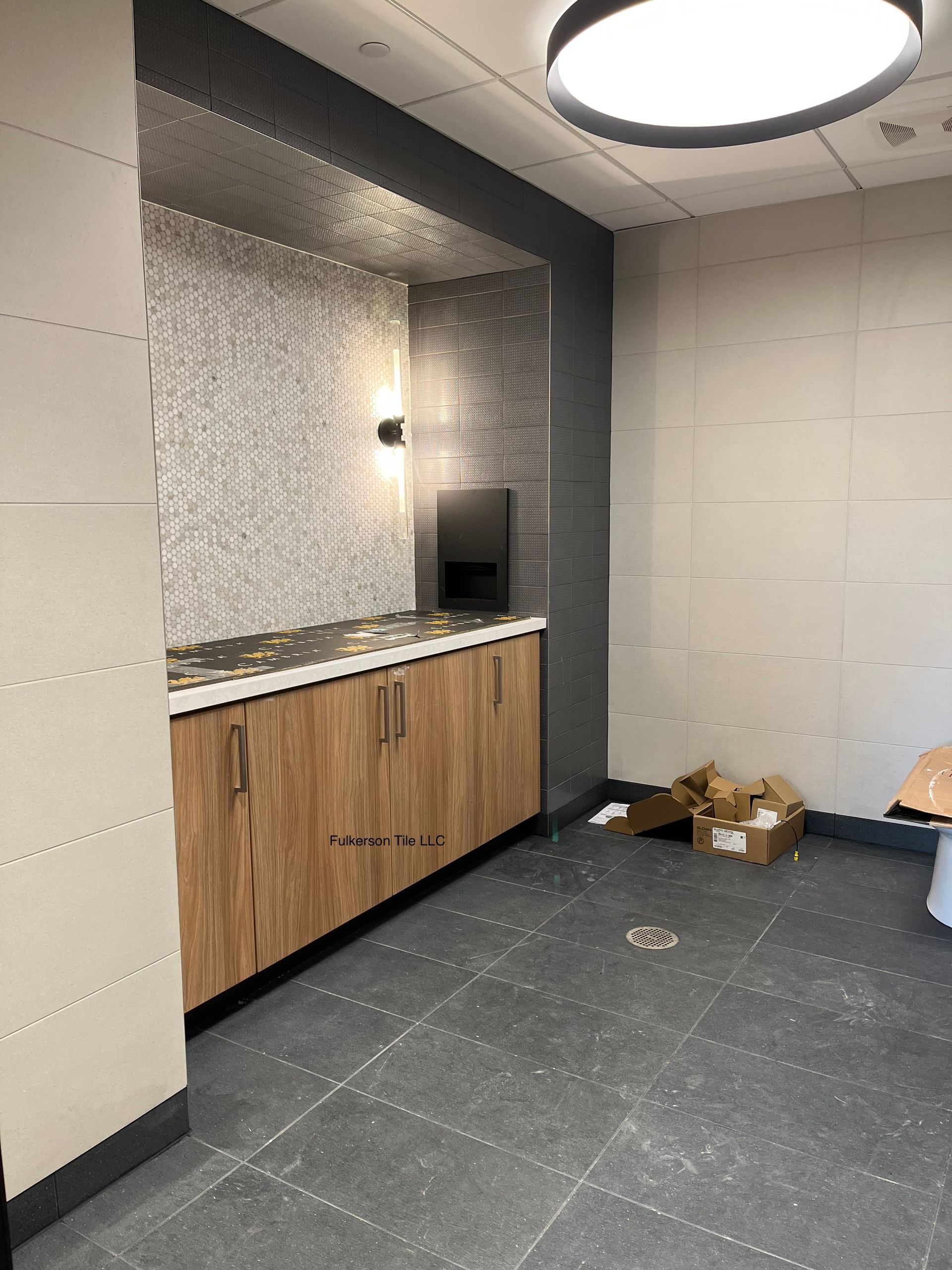 A newly constructed room with a vanity and cabinets. Gray tile floor, light walls, and wood-tone cabinets.