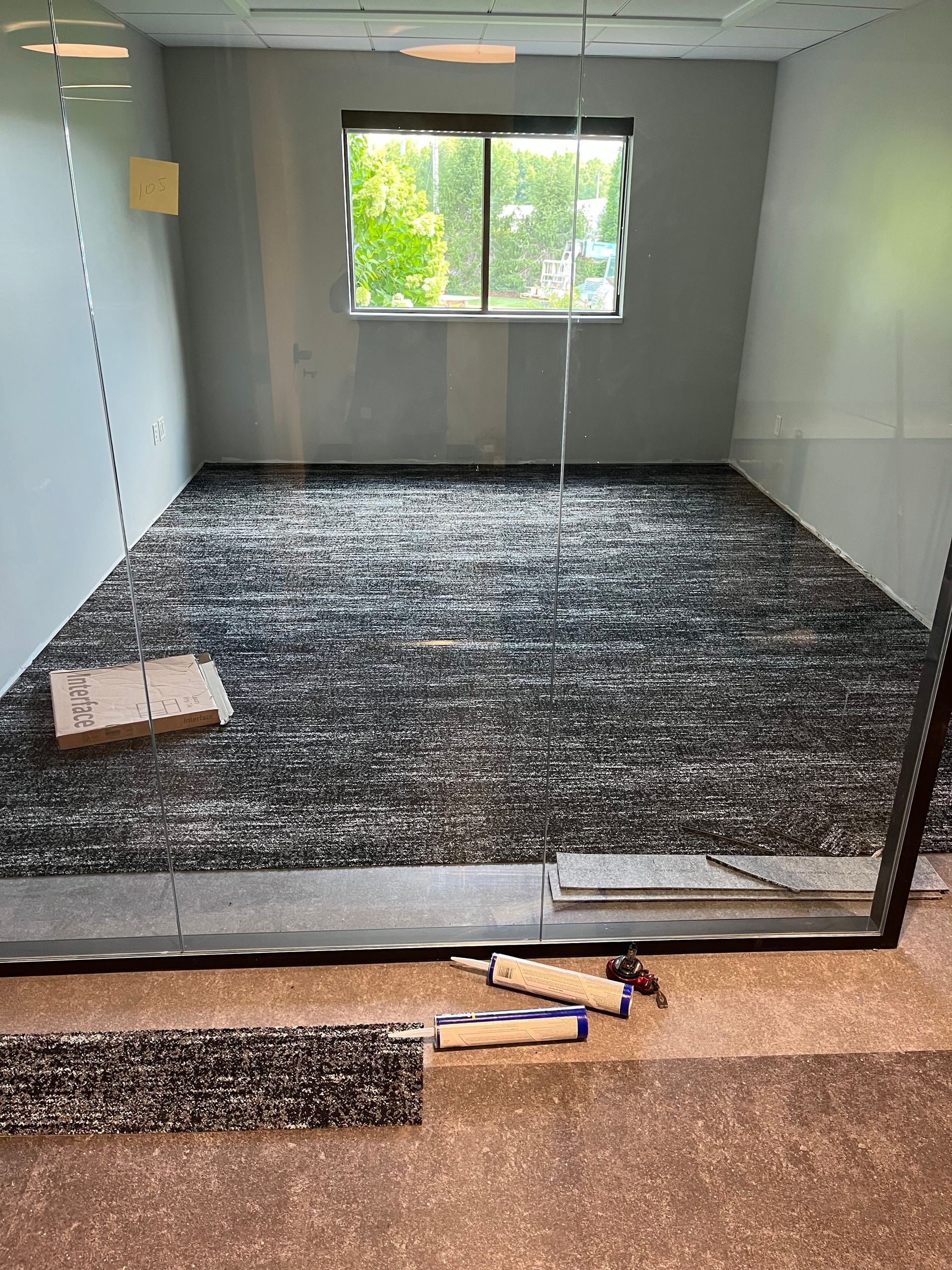 Room with partially installed black and gray flooring tiles, window, and tools.