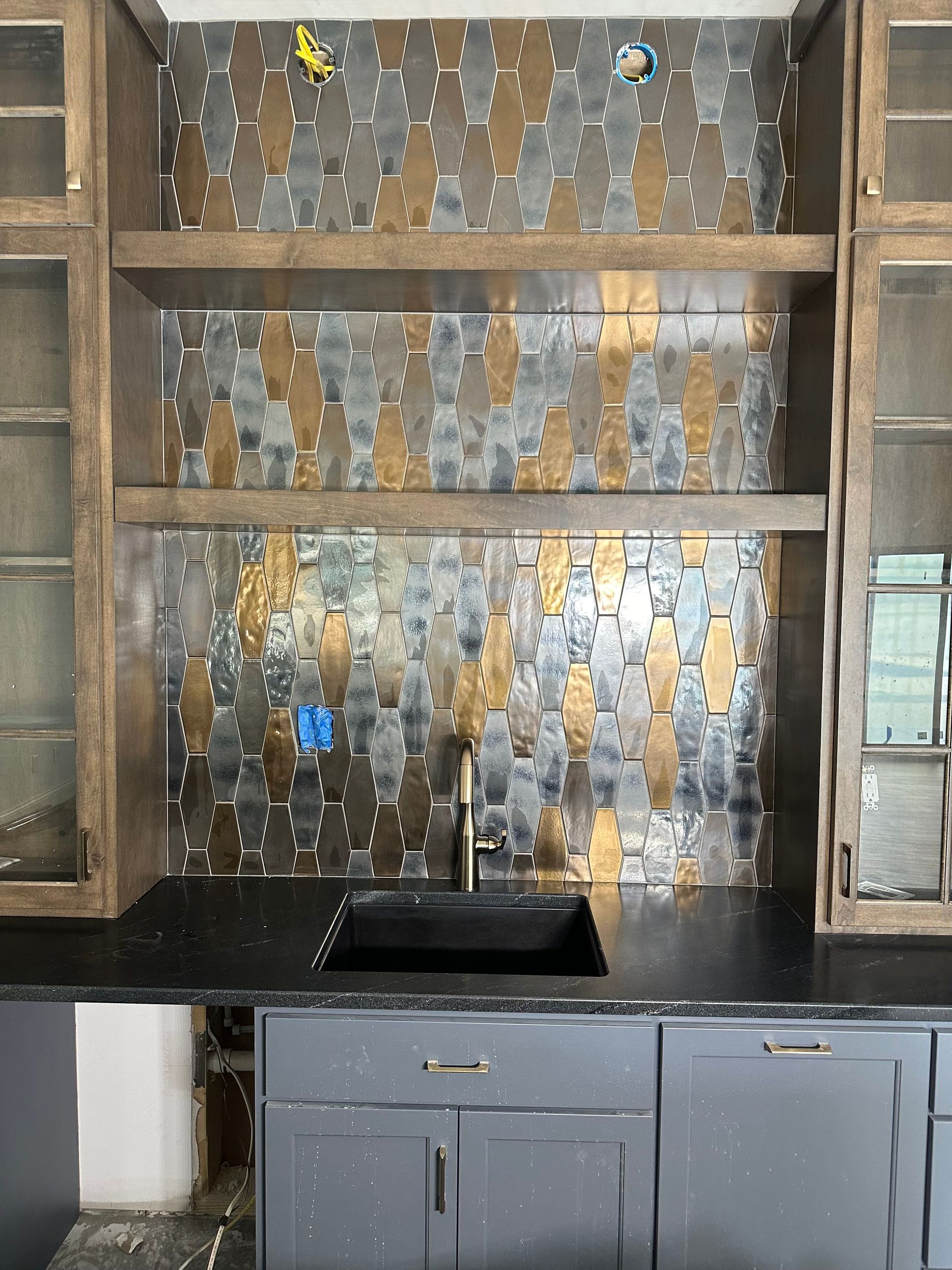 Kitchen with gray cabinets, black countertop, and a backsplash with metal tiles; shelves, sink.