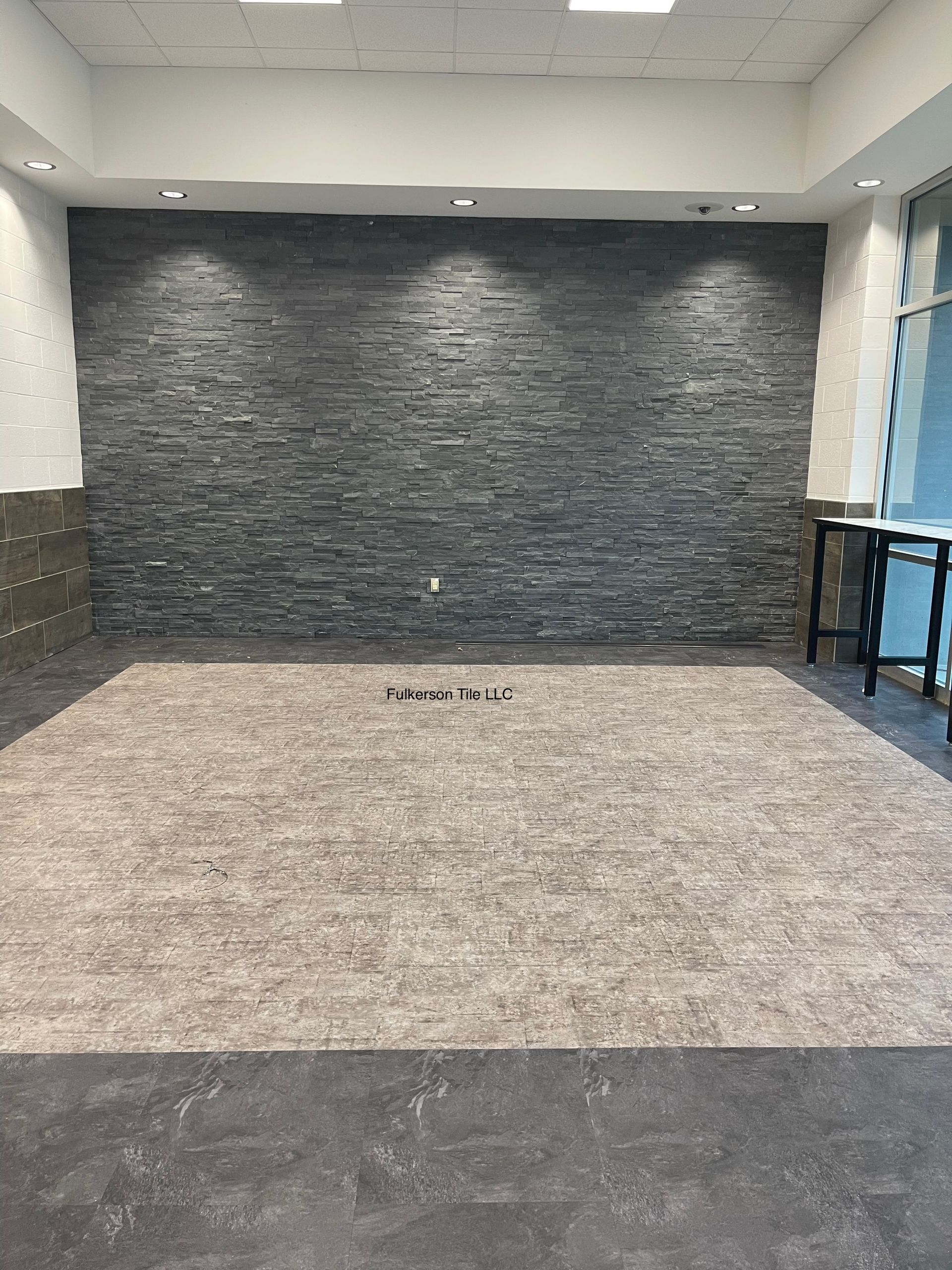 Empty room with gray stone accent wall, recessed lighting, and beige carpet.