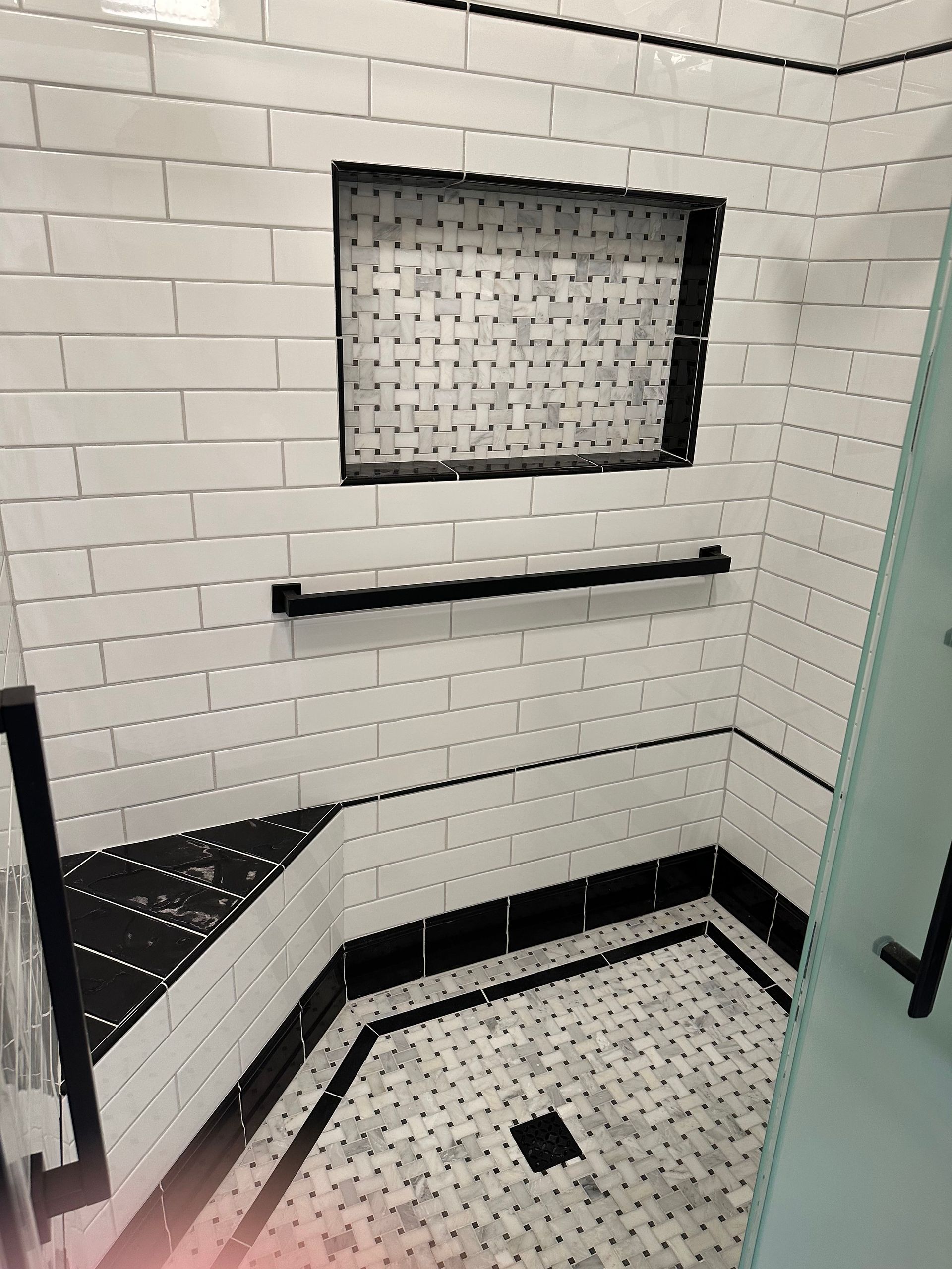 White tiled shower with black accents, including a built-in shelf and a soap niche.