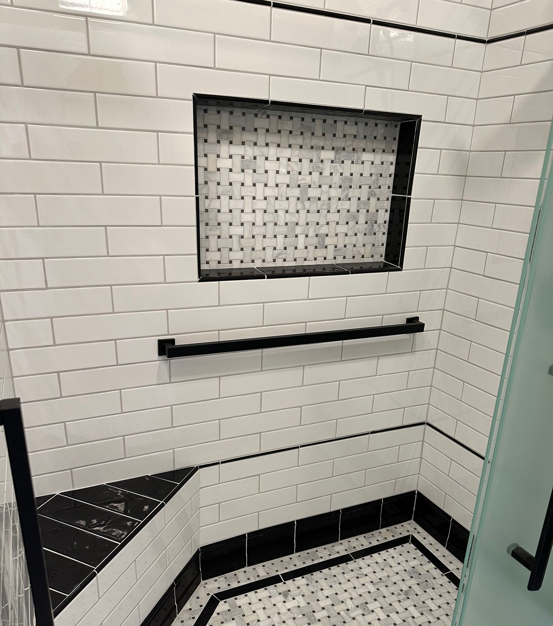 Shower with white subway tile, black accents, built-in shelf and alcove.