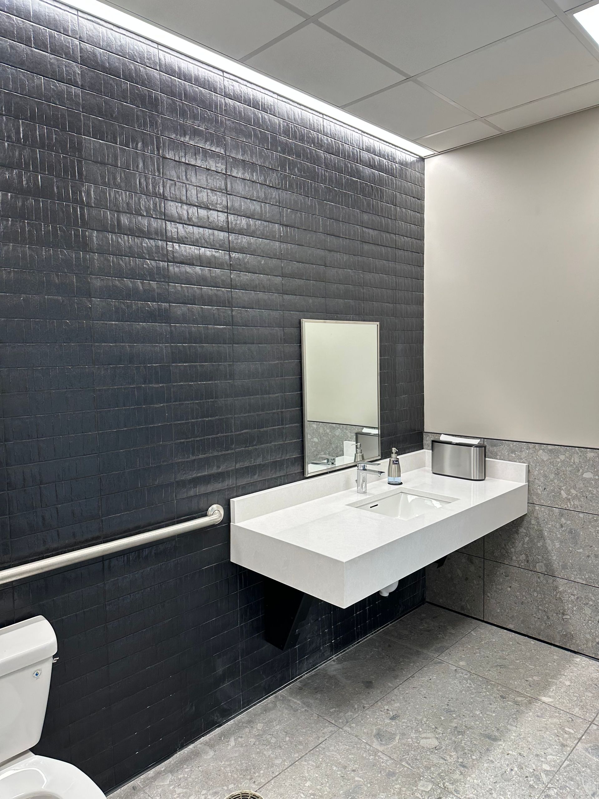 Modern, accessible restroom with floating sink, dark tiled wall, and silver fixtures.
