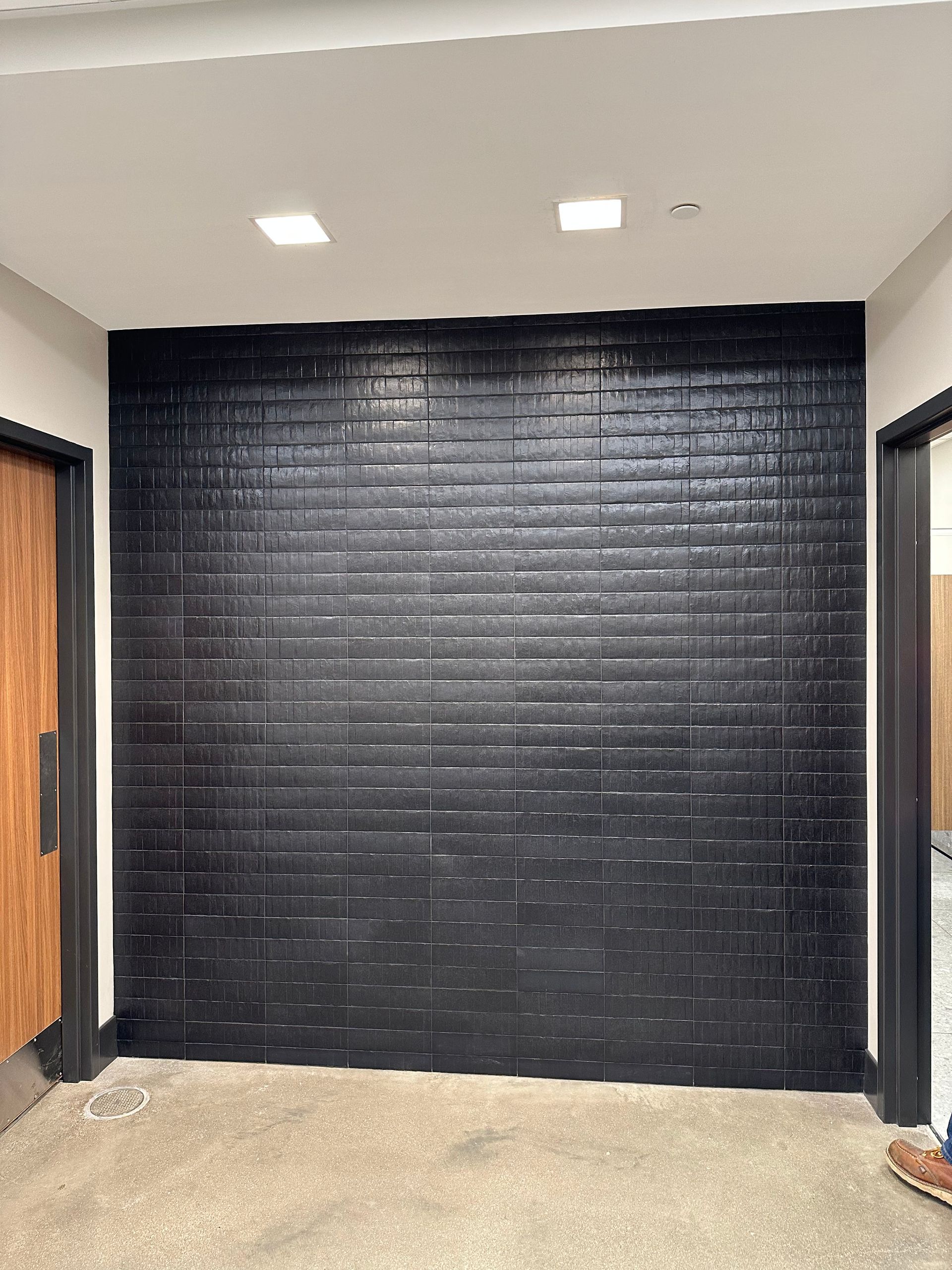 Black brick wall between two doorways with light fixtures above.