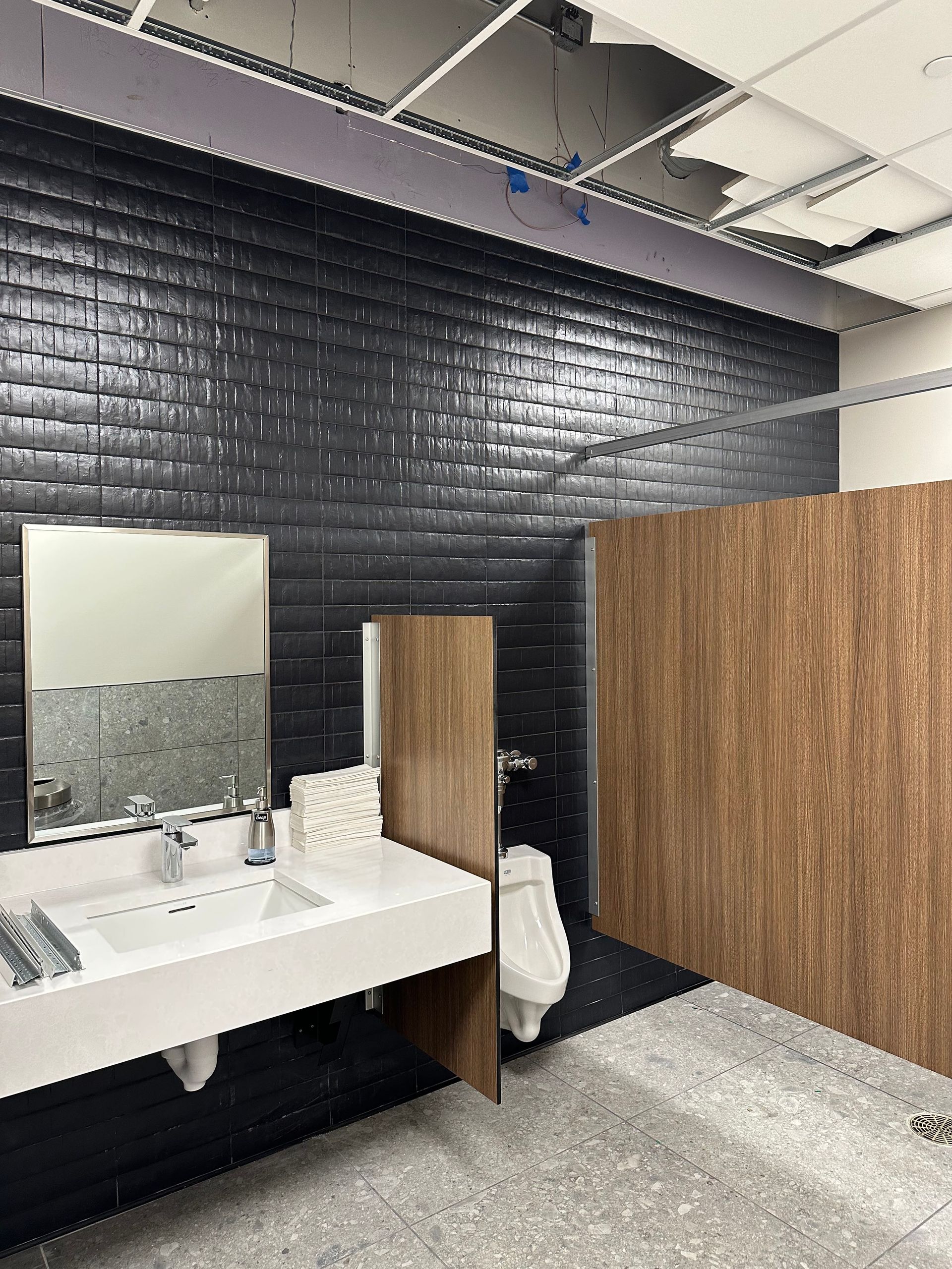 Bathroom with black tiled walls, a white sink, and wooden stall doors.