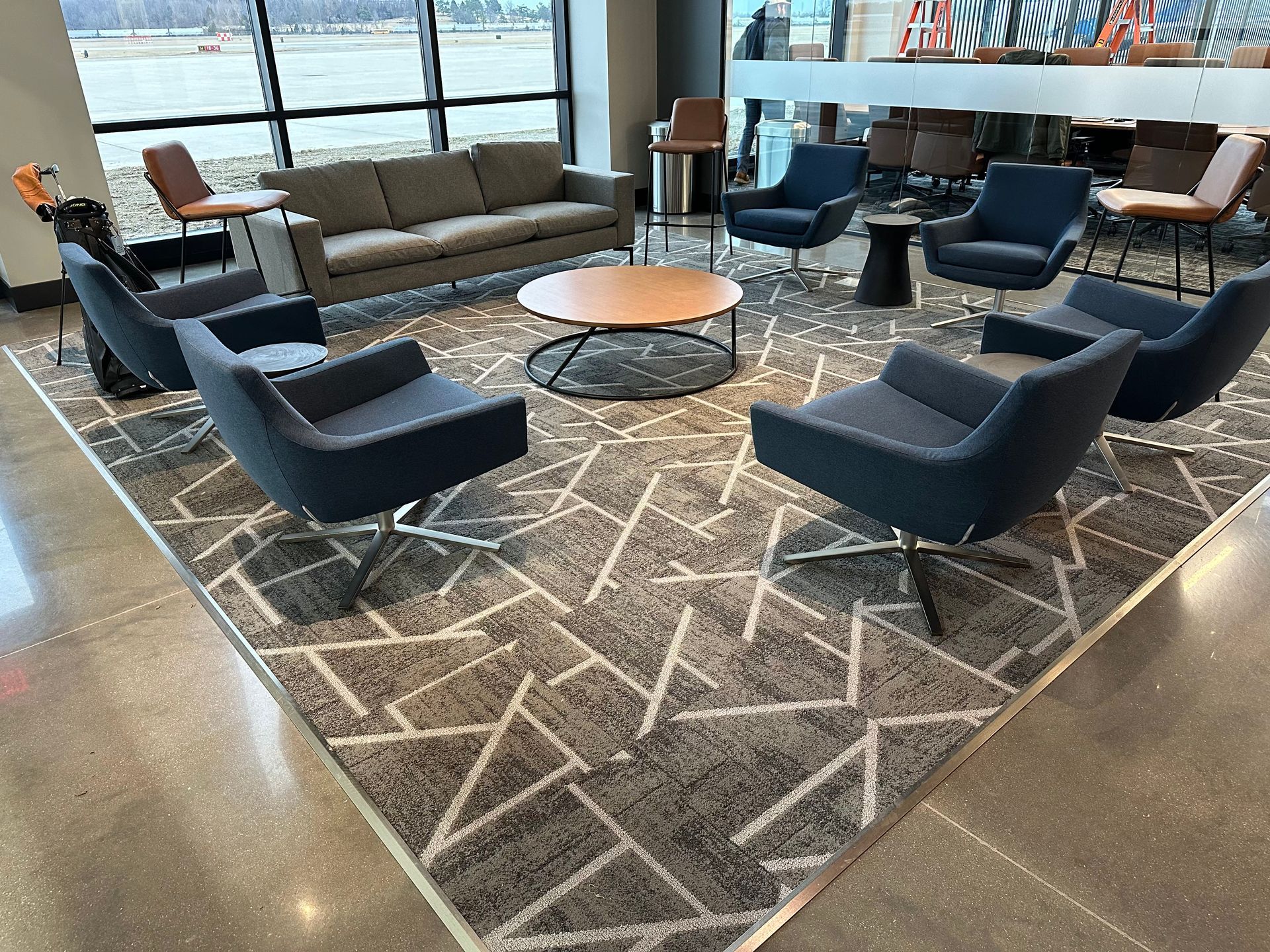 Lounge area with gray sofa, blue chairs around a coffee table on a patterned rug near a window.