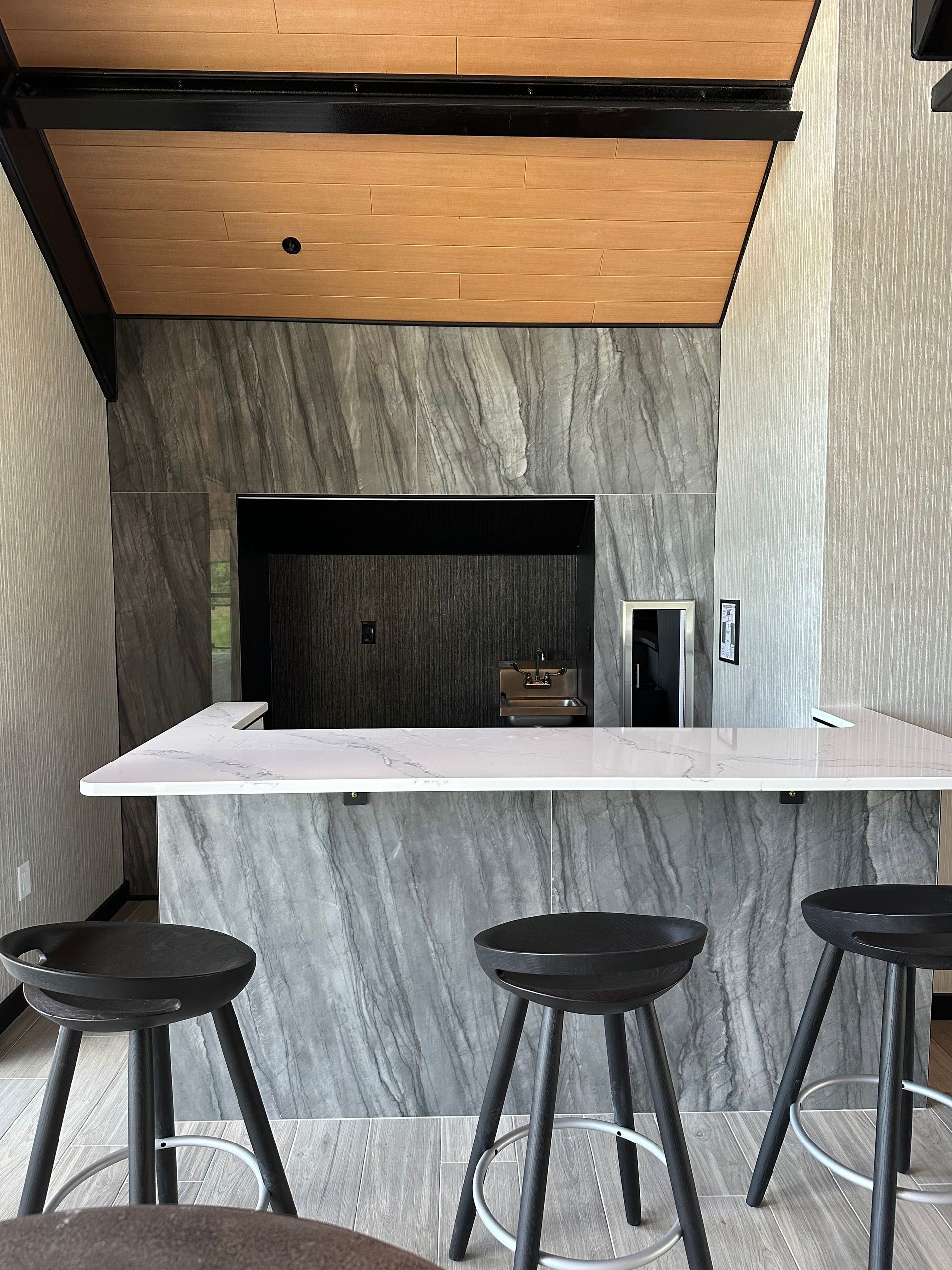 Bar area with marble-look walls, wooden ceiling, white countertop, black stools.
