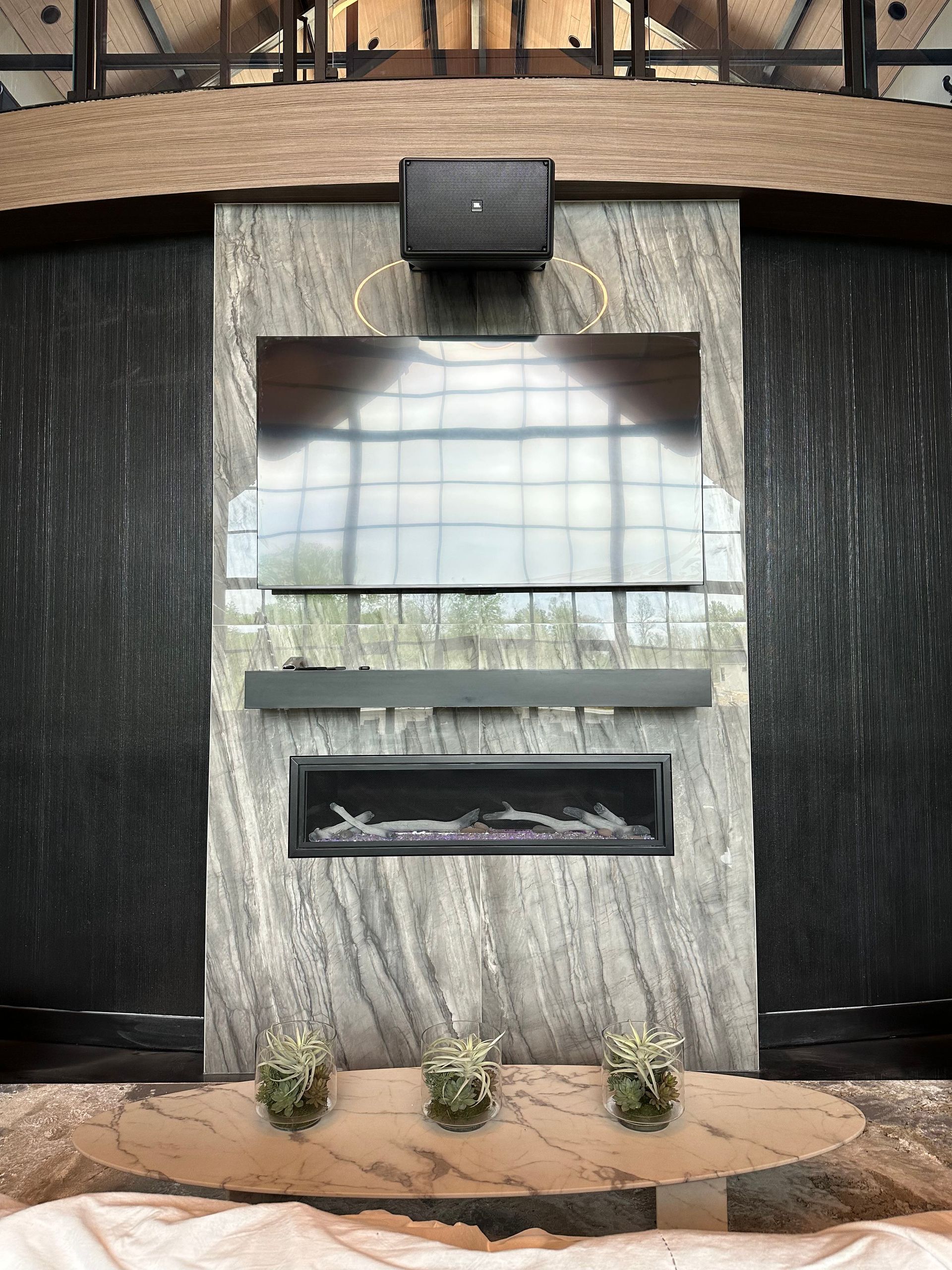 Stone fireplace with TV, soundbar, and decorative plants. Black panels flank the fireplace.