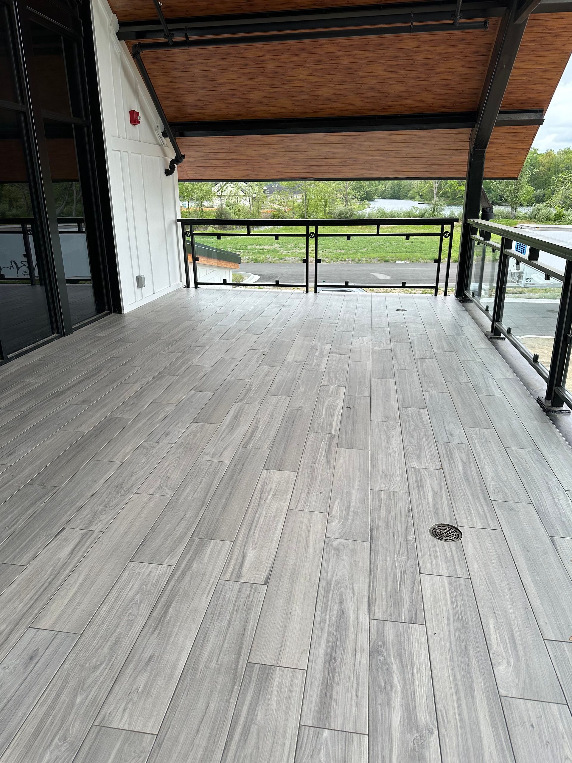 Wooden deck with glass railing, under a wood-paneled overhang.