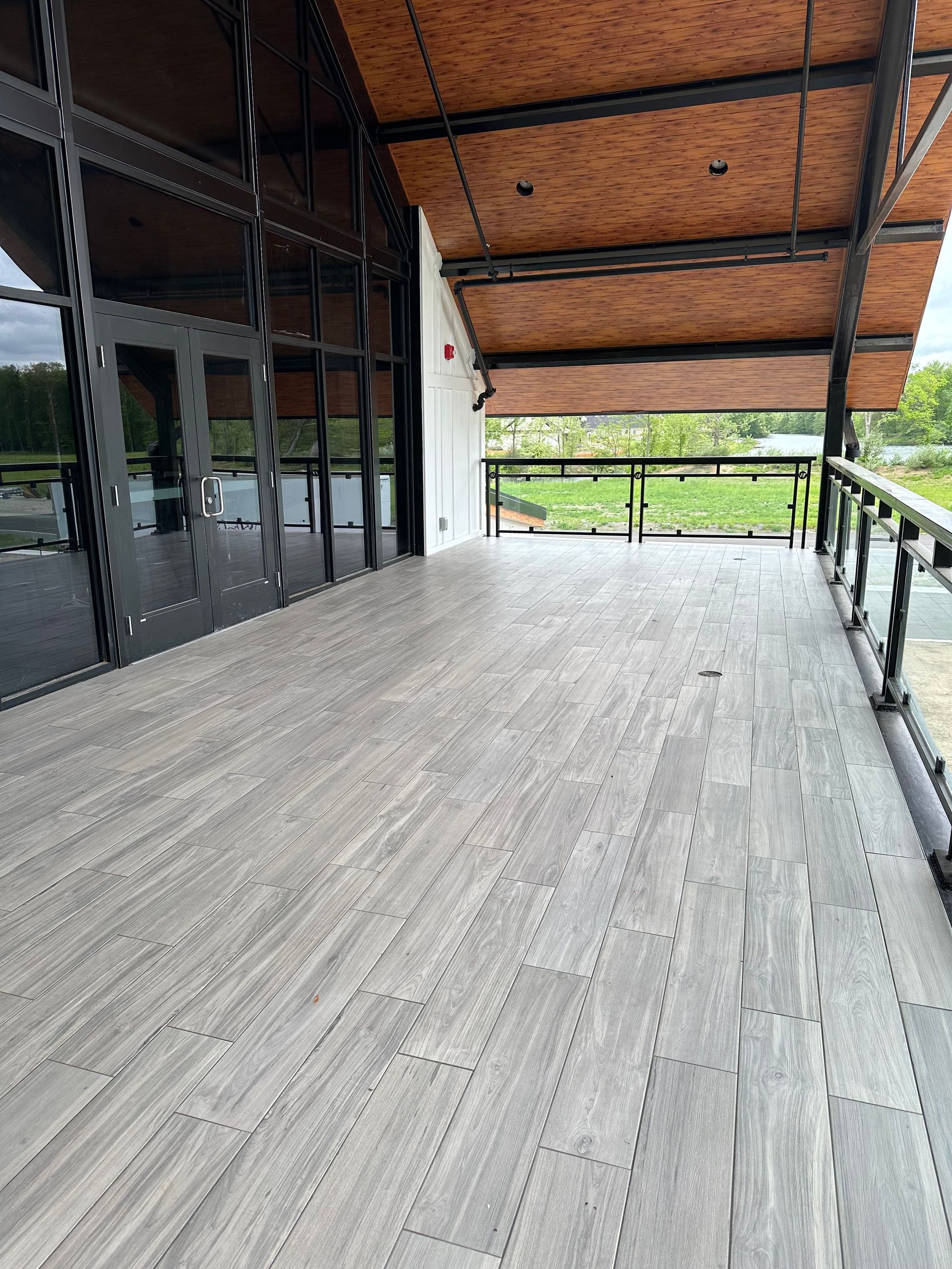 Exterior deck with grey tile flooring, glass walls, and a wooden ceiling.