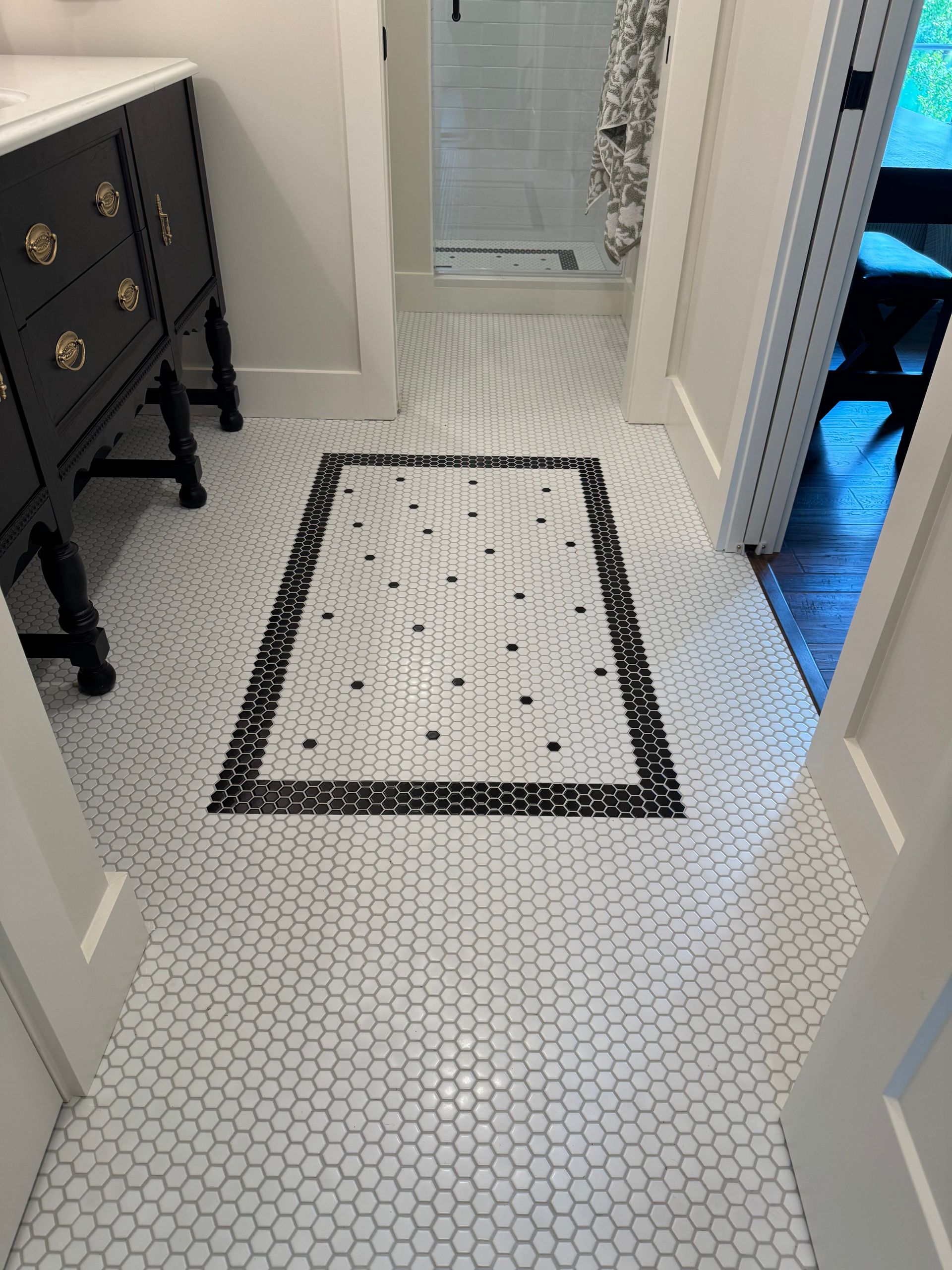 Bathroom with white hexagonal floor tiles. Black and white patterned accent in center. Dark wood vanity on the left.