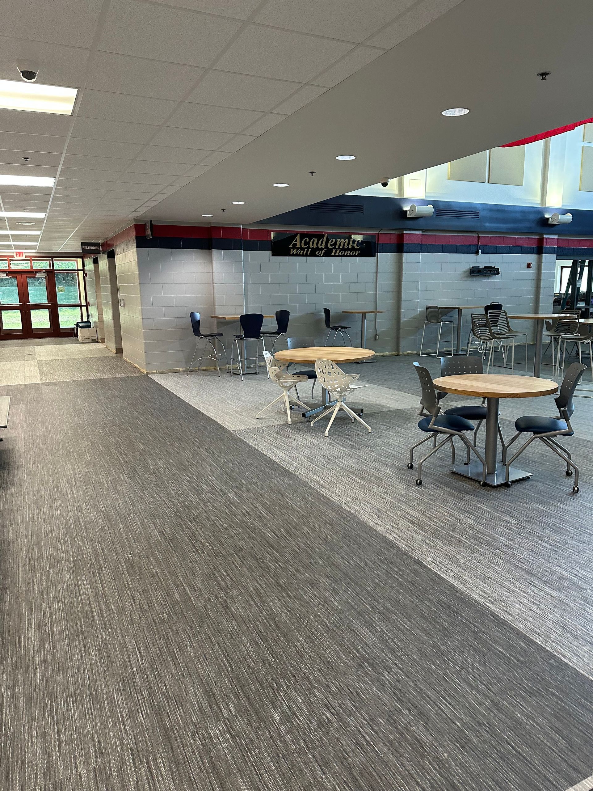 Empty school cafeteria with tables, chairs, and a small sign above.
