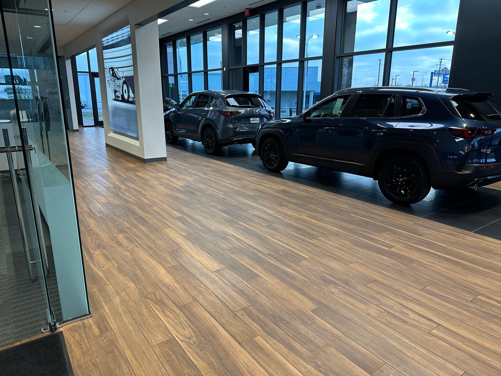 Two blue SUVs in a showroom with wood flooring and large windows, displaying cars for sale.