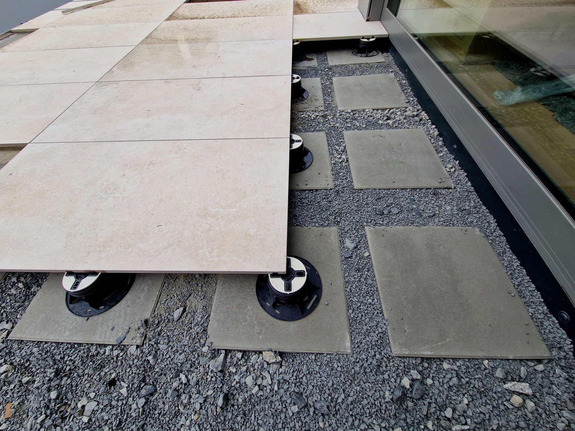 Raised patio tiles on adjustable supports over gravel and smaller stepping stones.