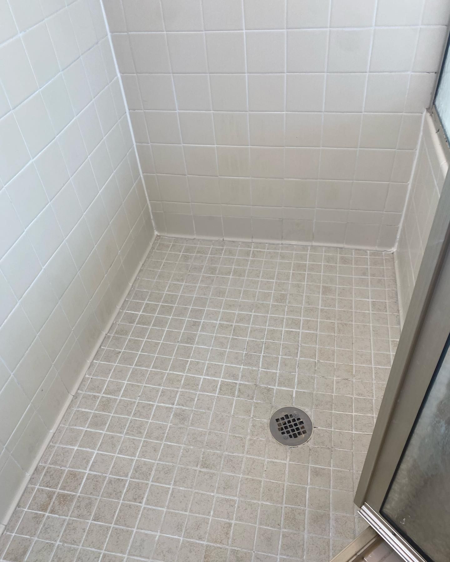 A shower stall with white tiles and a drain.