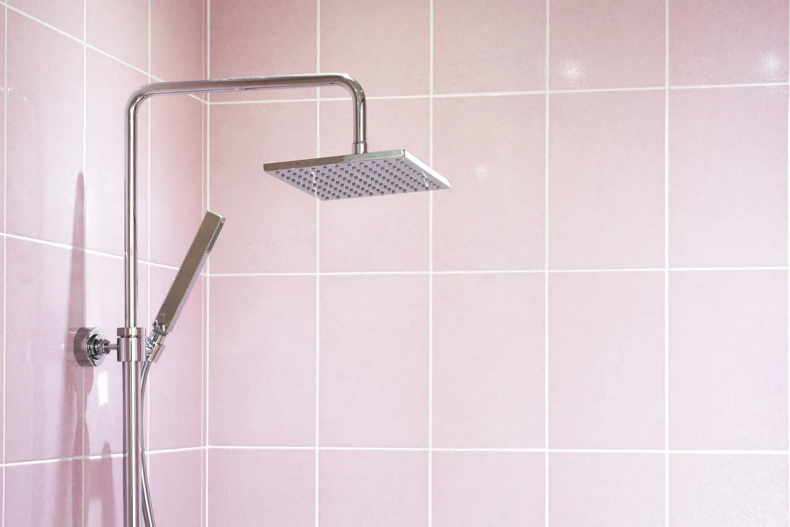There is a shower head in the shower with pink tiles.