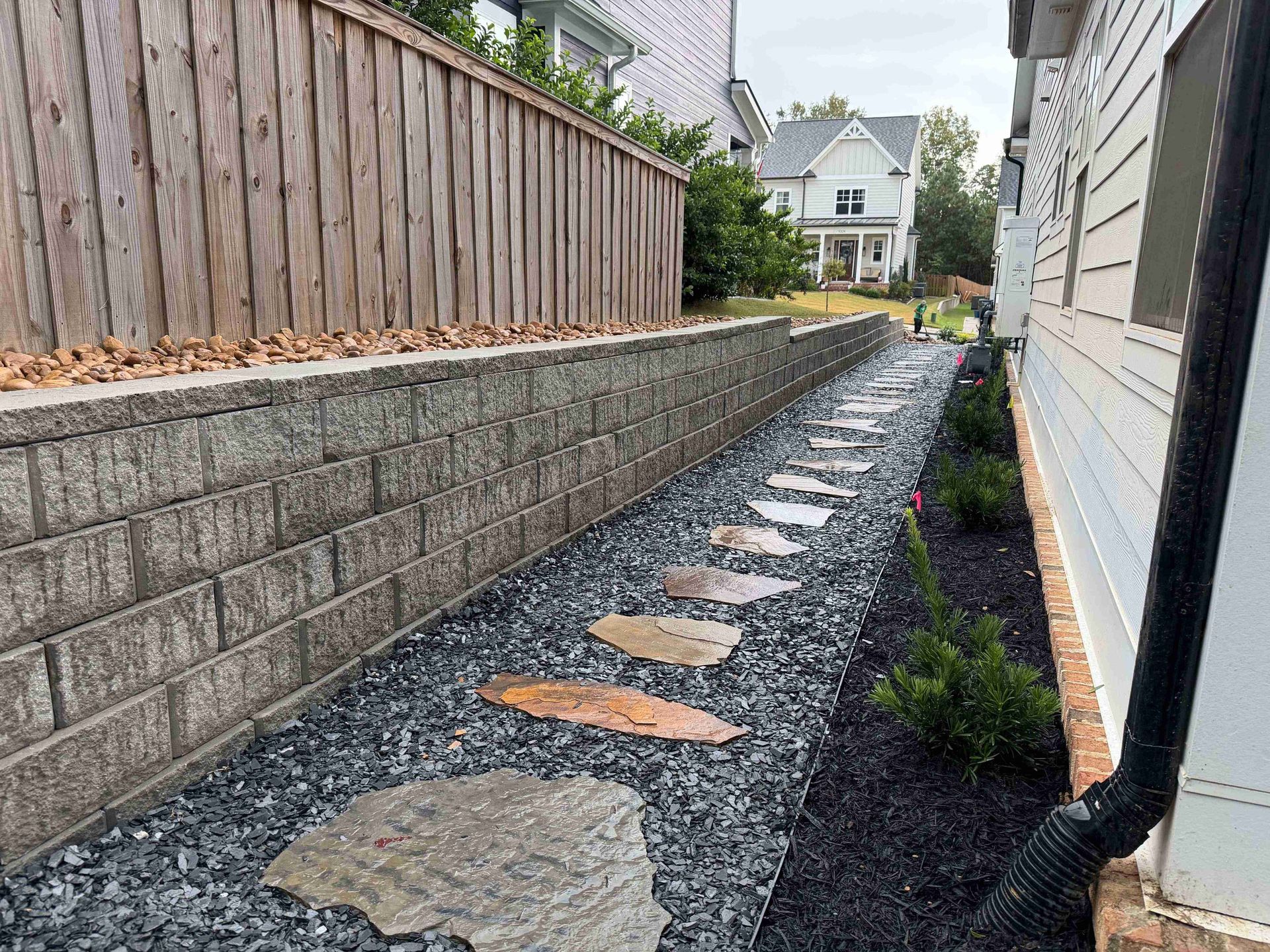 Stone pathway between a retaining wall and house, with black mulch, gravel, and steps.