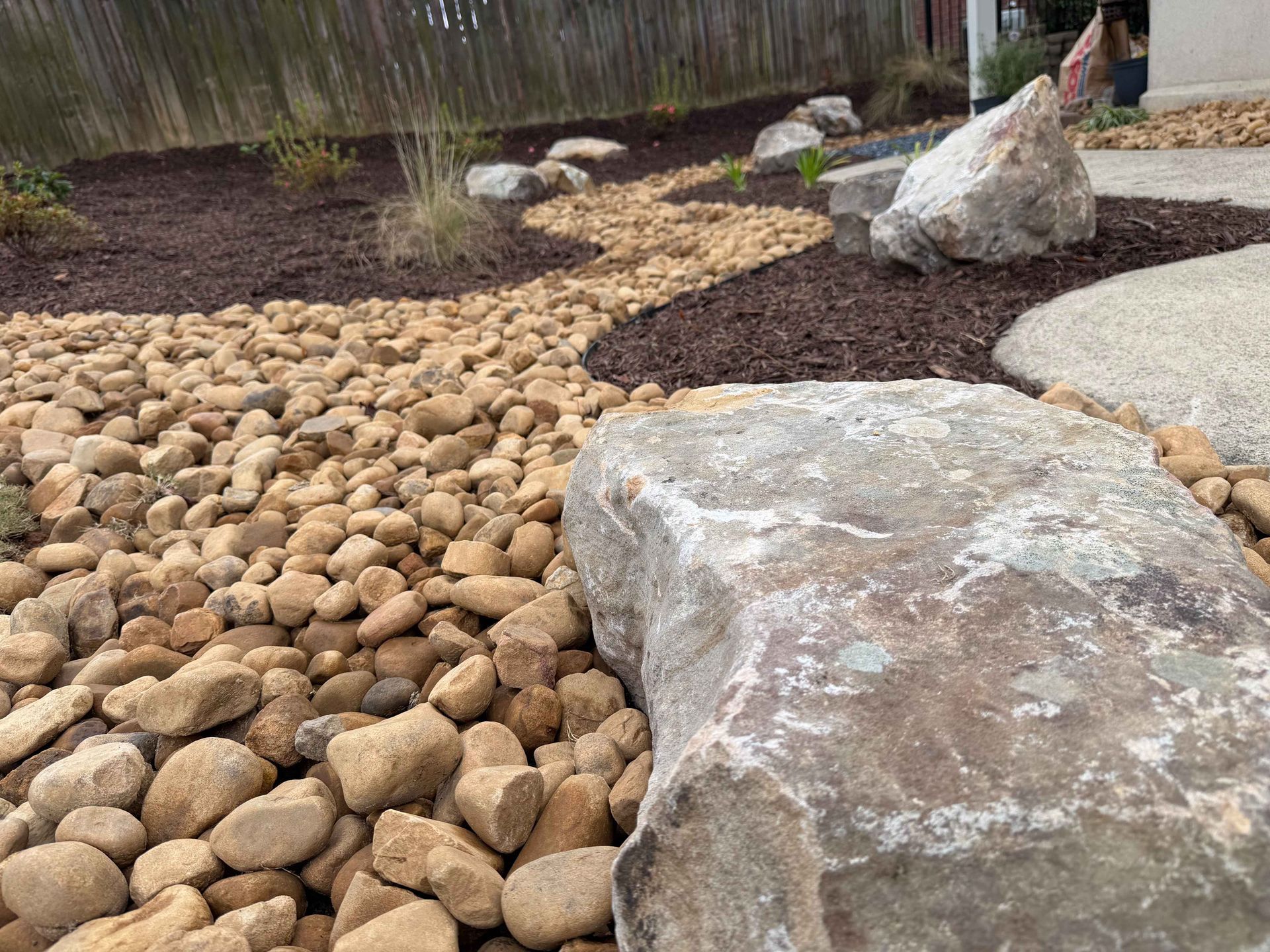 Rock landscaping with brown pebbles and dark mulch, large stones, and a wooden fence.