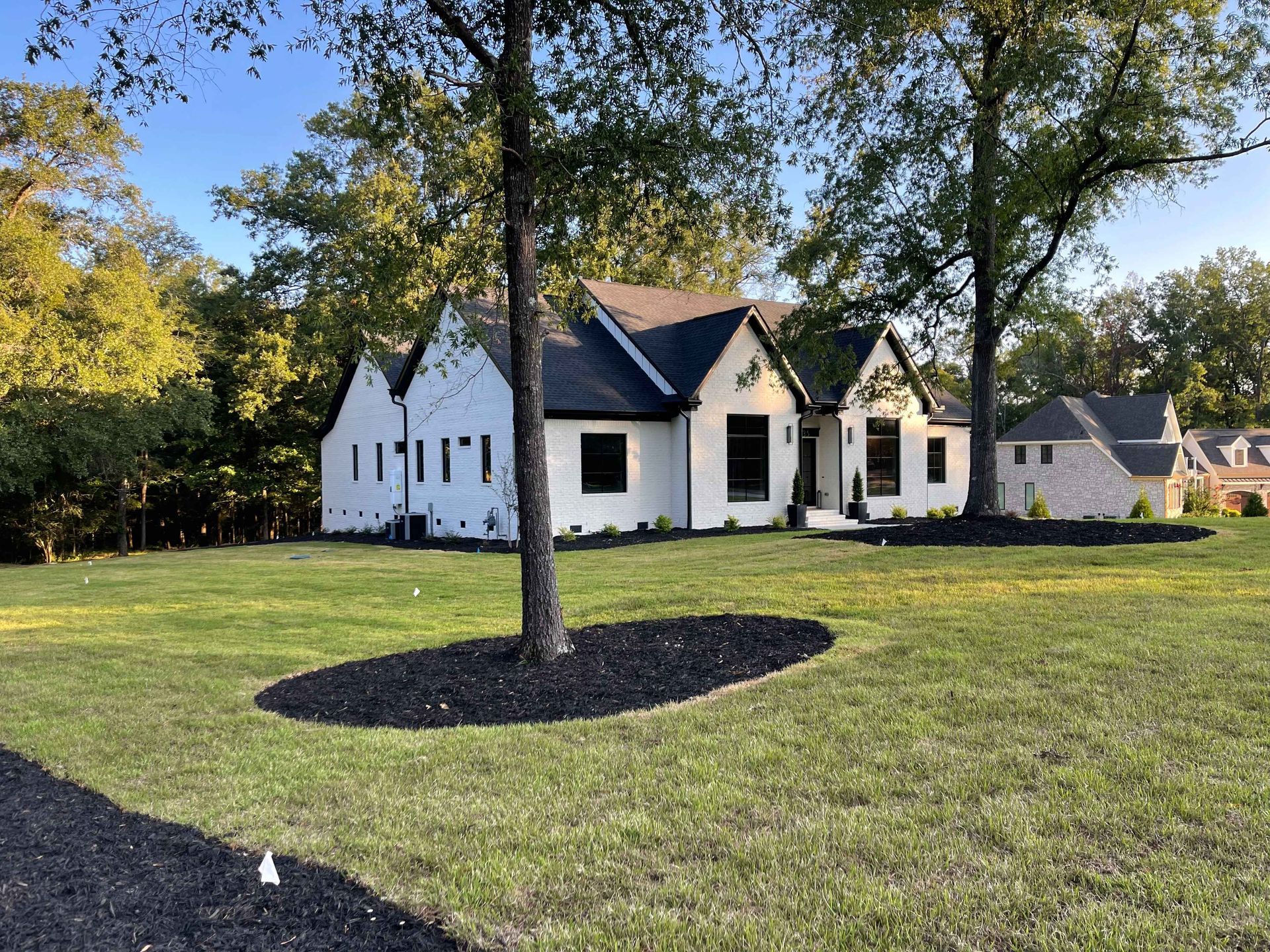 White house with black trim, trees, green lawn.