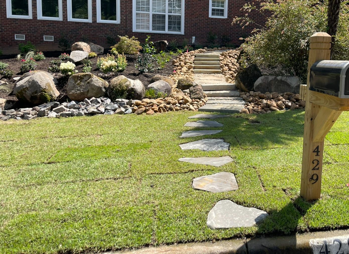 A stone path leads to steps up a landscaped yard. A mailbox and house are visible.