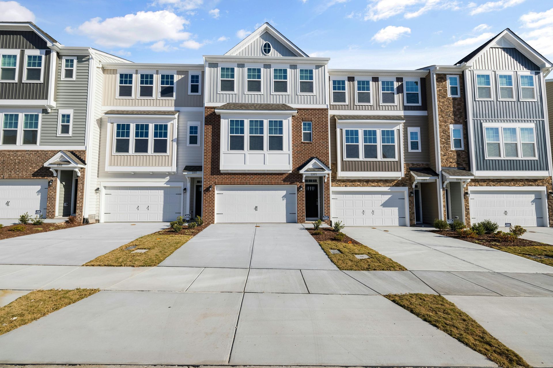 Row of modern townhomes with white, brown, and gray exteriors, each with a garage and driveway.