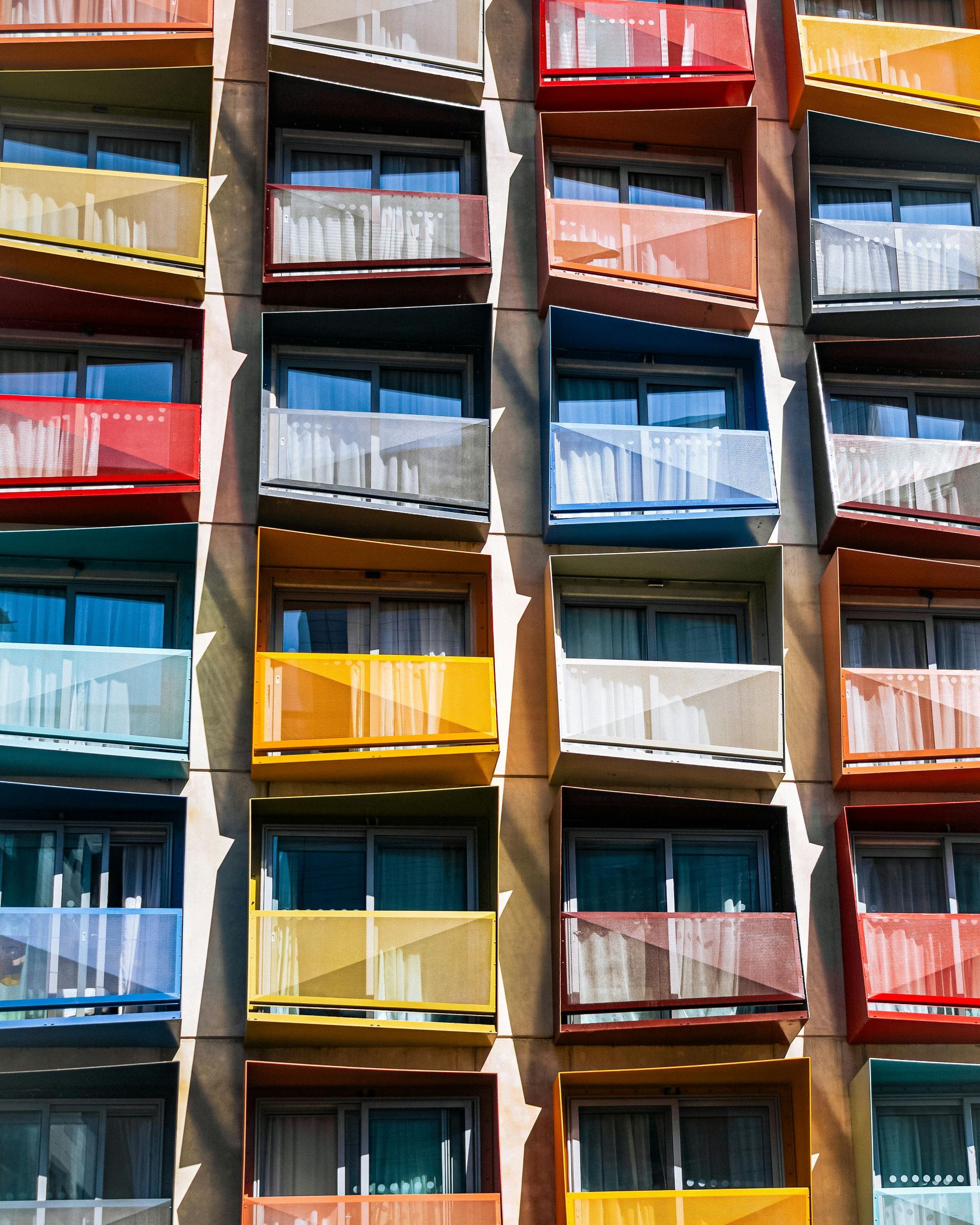 Colorful building facade with a grid of balconies. Red, blue, yellow, and orange railings.