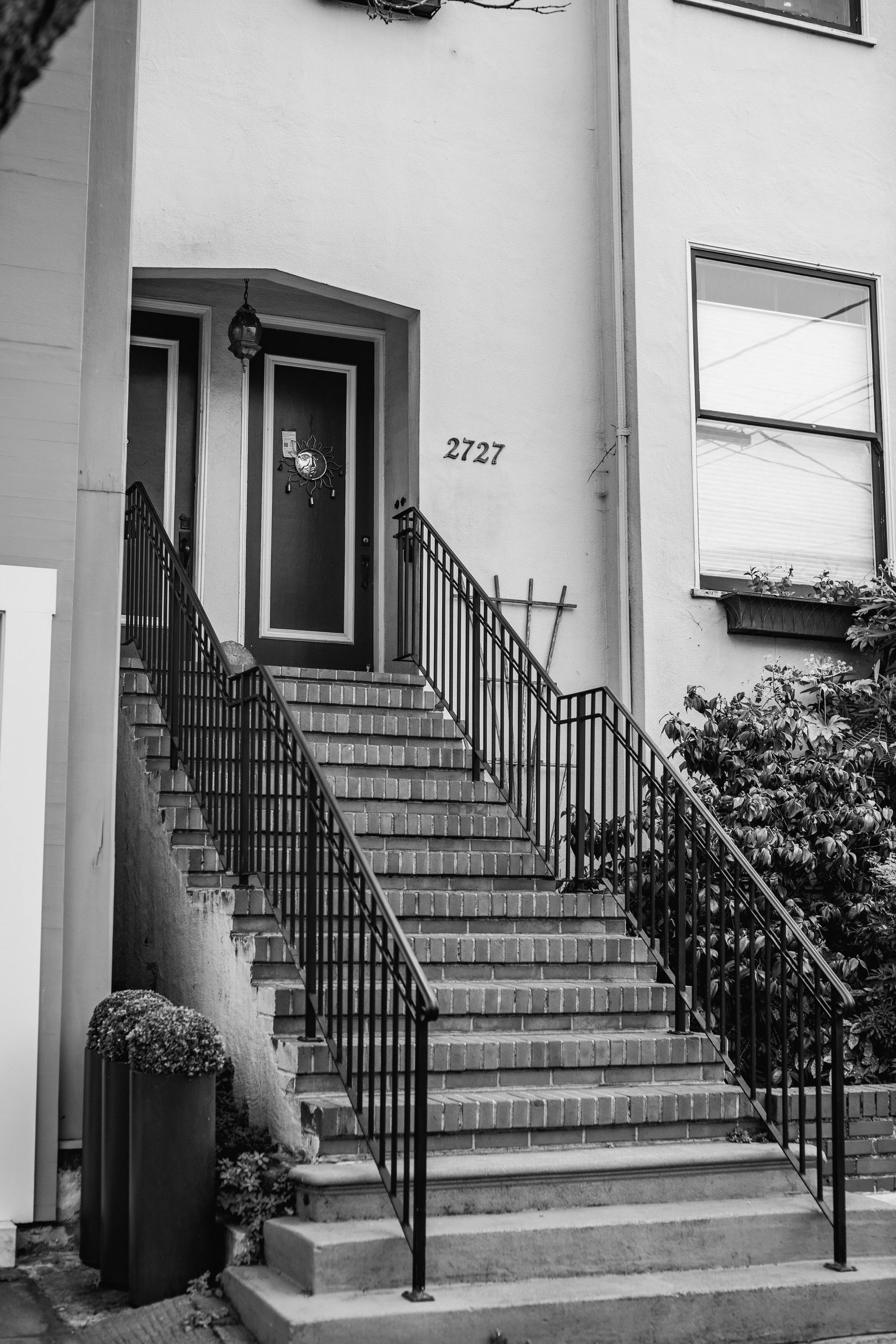 Stairway leading up to a house entrance with black railings, a door, and a partially visible window.