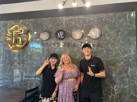 Three people pose in front of a wall with Chinese characters and a tiger logo. They are smiling.
