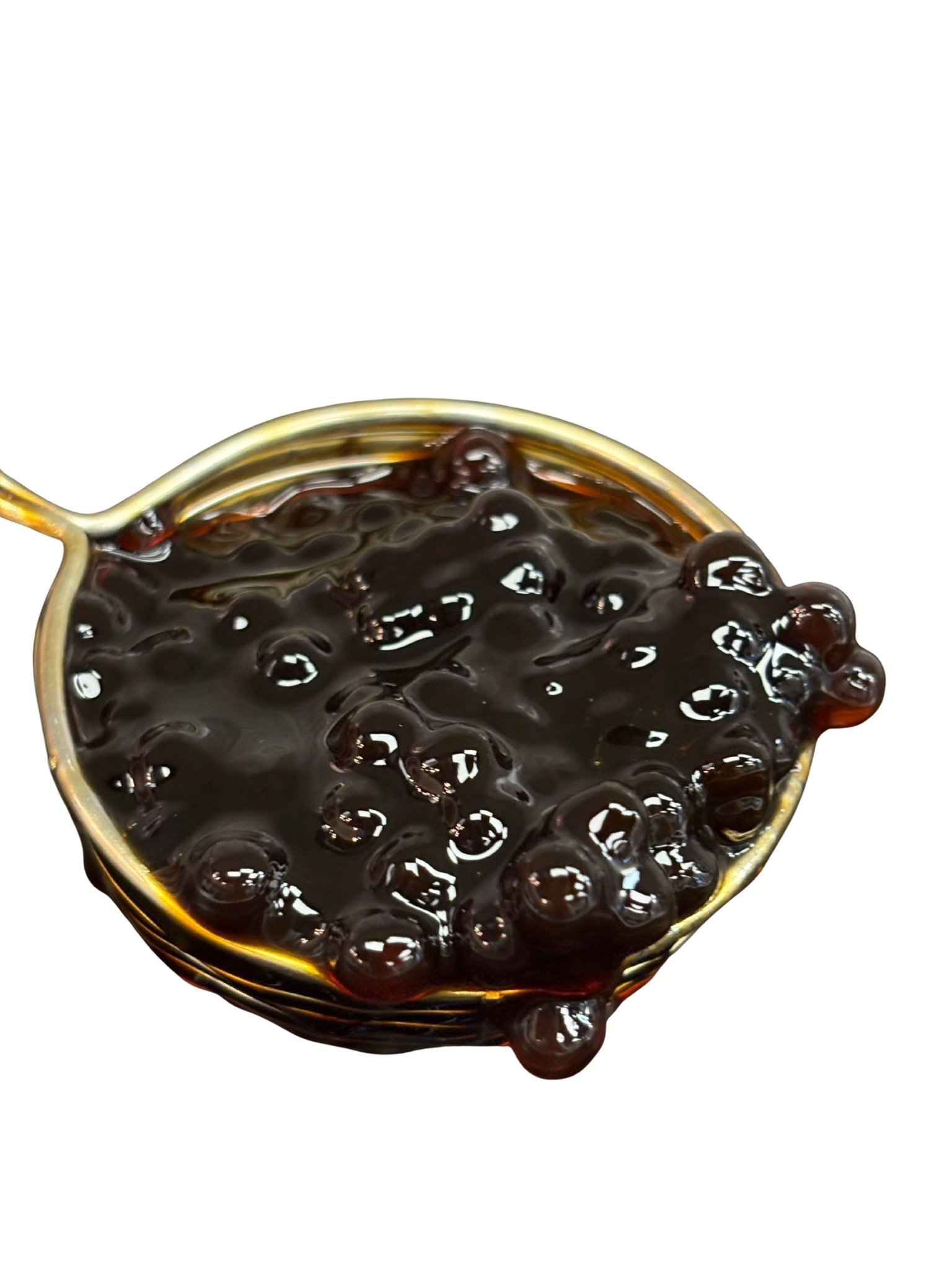 Dark brown boba pearls in a gold spoon. Some pearls are spilling over the side.