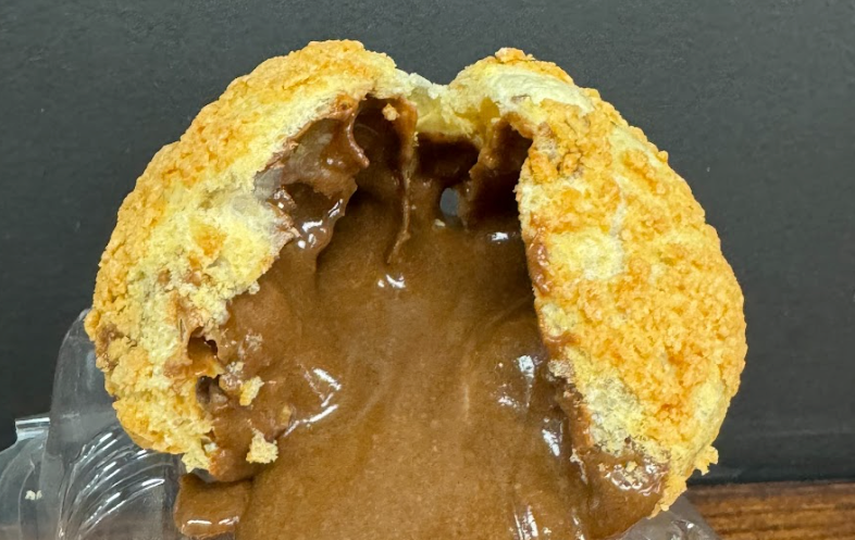 Half a pastry with a golden, crunchy top, overflowing with thick, dark chocolate filling against a dark background.