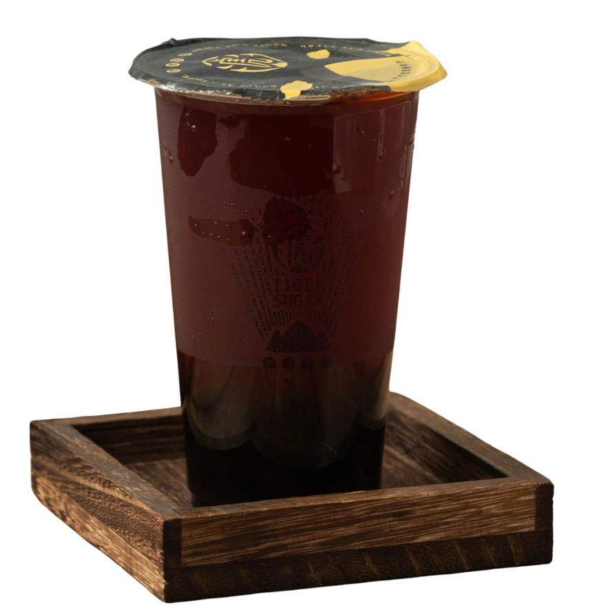 Dark tea in a clear plastic cup with a sealed lid, sitting on a square wooden tray.