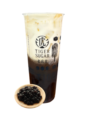 Tiger Sugar boba drink with brown sugar syrup, cream, and tapioca pearls in a clear cup with a small wooden dish of pearls.