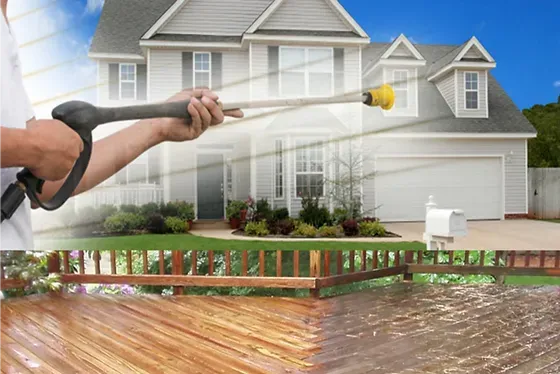 A man is spraying water on a wooden deck in front of a house.