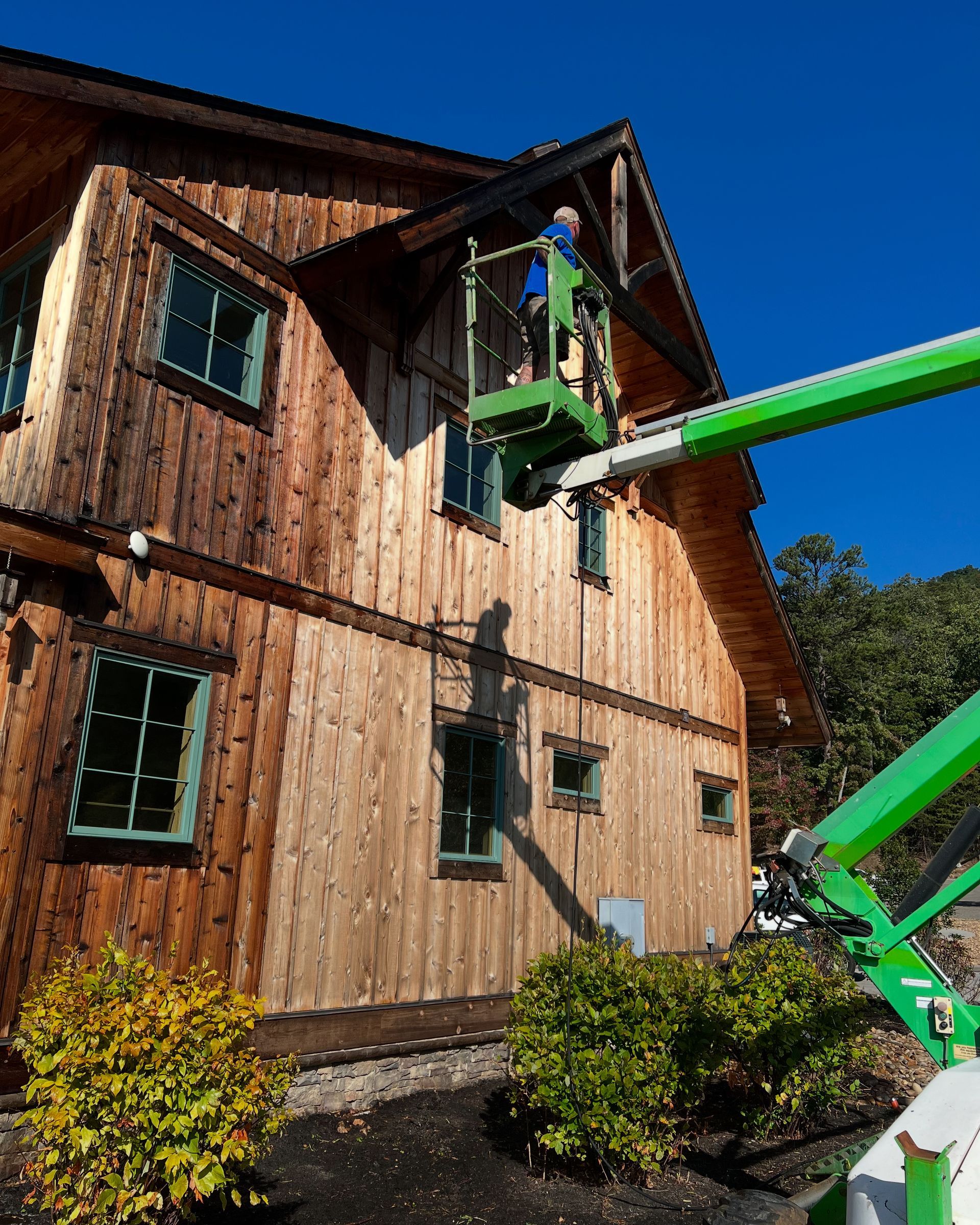A man is standing in a green bucket on top of a wooden house.