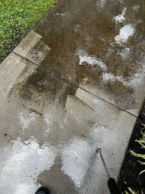 A person is cleaning a sidewalk with a pressure washer.
