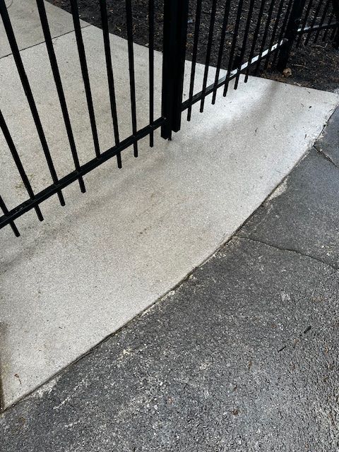 A black fence is surrounding a concrete walkway.Cleaning by 865 Power Wash