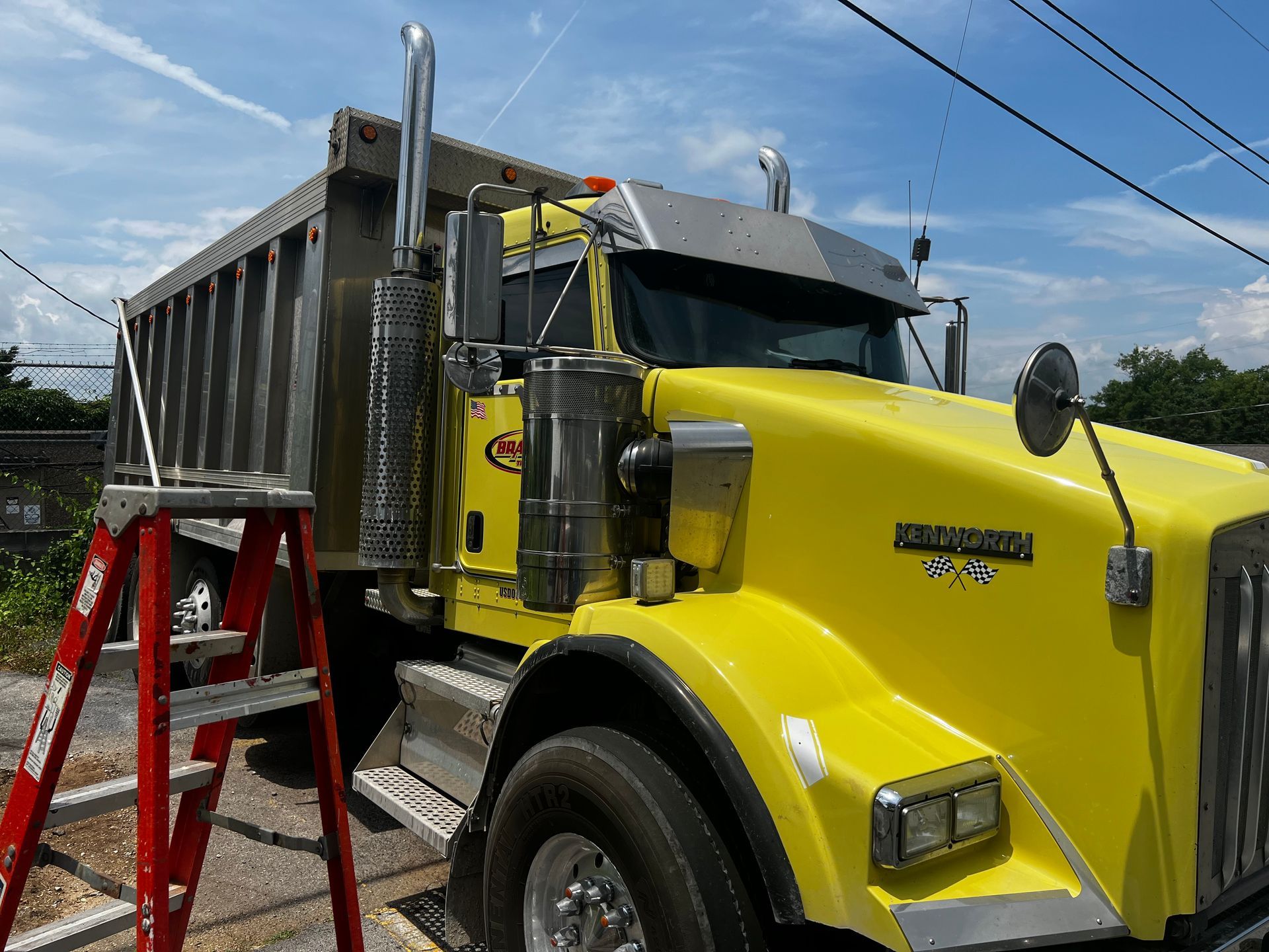 A yellow dump truck is parked next to a red ladder