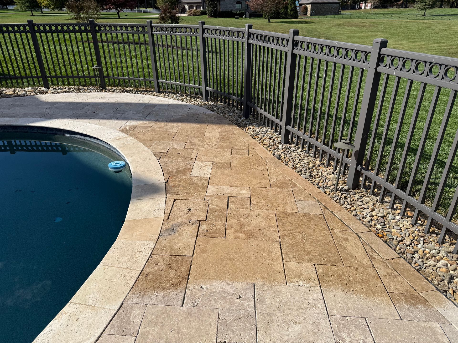 A fence surrounds a swimming pool with a brick walkway leading to it.