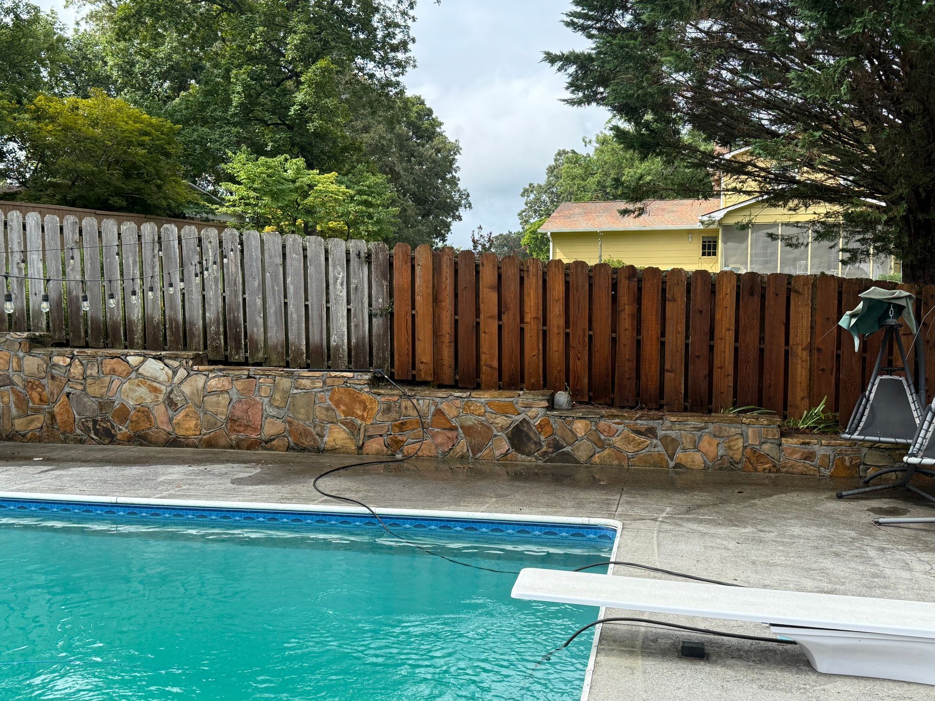 Swimming pool with a diving board, stone wall, and wooden fence.