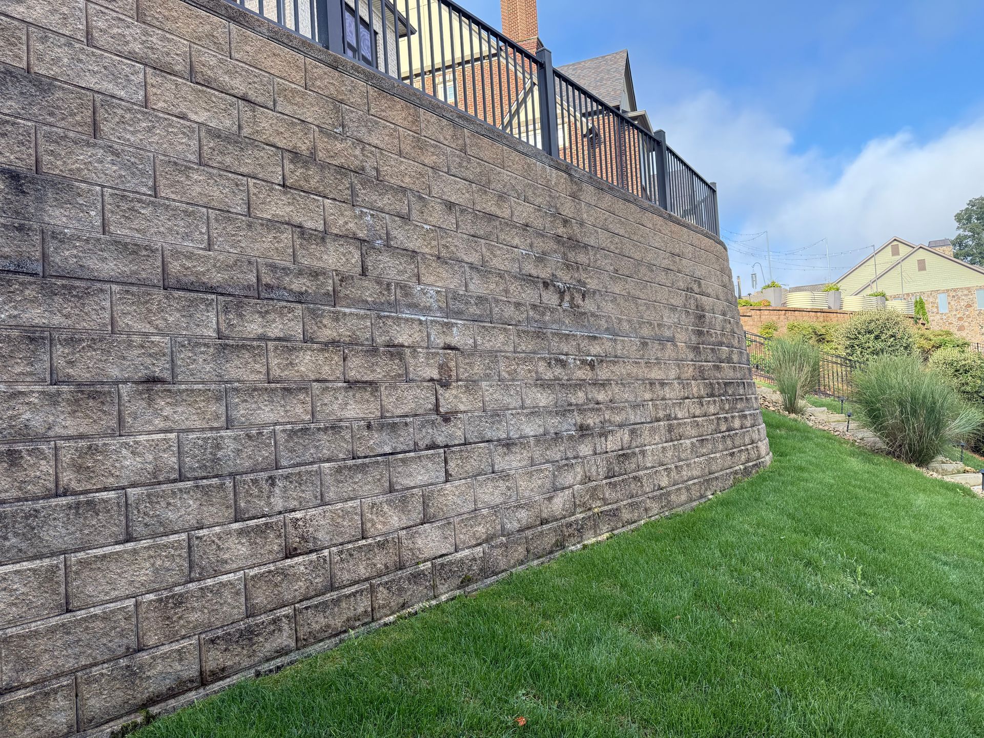 A large retaining wall made of textured blocks, with green grass in front and a house visible above.