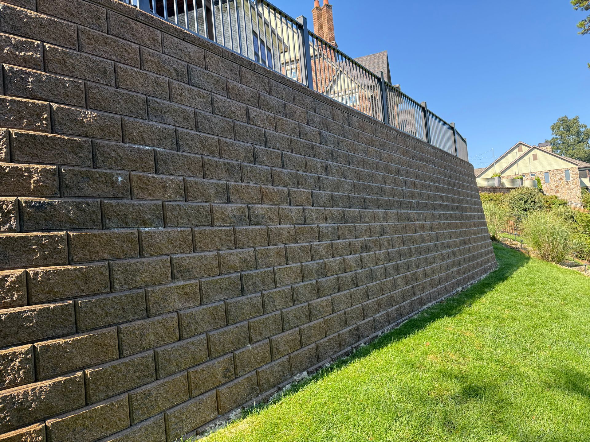 Brown retaining wall with a grassy yard and a house in the background.